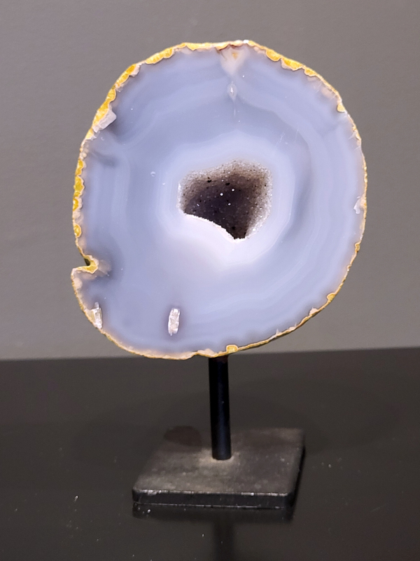 Agaat op standaard, 772 gram, 15cm hg. en 9cm br.  27,- euro, nr. 12
Agaat is een veelzijdige edelsteen die bekend staat om zijn prachtige kleurbanden en patronen. Het is een variëteit van het mineraal kwarts, meer specifiek chalcedoon, en wordt vaak gebruikt in sieraden en als decoratieve steen. 
Algemene kenmerken:
Agaat is een microkristallijne vorm van kwarts, bestaande uit microscopisch kleine kristallen. 
Kleuren en patronen:
Agaat komt voor in vele kleuren, vaak met banden of lagen in verschillende tinten. 
Agaat is een populaire keuze voor het maken van kettingen, armbanden, ringen en andere sieraden vanwege de esthetische aantrekkingskracht en duurzaamheid. 
Spirituele eigenschappen:
Agaat wordt vaak geassocieerd met aardende, stabiliserende en beschermende eigenschappen. 
Helende werking:
Er wordt aangenomen dat agaat kan helpen bij het verminderen van stress, het bevorderen van emotioneel evenwicht en het versterken van het zelfvertrouwen. 
Verzorging van agaat:
Agaat is relatief gemakkelijk te onderhouden. Het kan worden gereinigd met lauw water, de rook van witte salie of palo santo, of door het op een hematiet- of bergkristal-cluster te plaatsen. 

-	Kunstgalerie-Arnold -