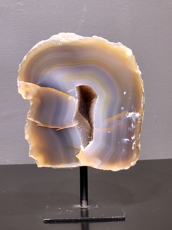 Agaat op standaard, 864 gram, 15cm hg. en 10cm br.  30,- euro, nr. 13
Agaat is een veelzijdige edelsteen die bekend staat om zijn prachtige kleurbanden en patronen. Het is een variëteit van het mineraal kwarts, meer specifiek chalcedoon, en wordt vaak gebruikt in sieraden en als decoratieve steen. 
Algemene kenmerken:
Agaat is een microkristallijne vorm van kwarts, bestaande uit microscopisch kleine kristallen. 
Kleuren en patronen:
Agaat komt voor in vele kleuren, vaak met banden of lagen in verschillende tinten. 
Agaat is een populaire keuze voor het maken van kettingen, armbanden, ringen en andere sieraden vanwege de esthetische aantrekkingskracht en duurzaamheid. 
Spirituele eigenschappen:
Agaat wordt vaak geassocieerd met aardende, stabiliserende en beschermende eigenschappen. 
Helende werking:
Er wordt aangenomen dat agaat kan helpen bij het verminderen van stress, het bevorderen van emotioneel evenwicht en het versterken van het zelfvertrouwen. 
Verzorging van agaat:
Agaat is relatief gemakkelijk te onderhouden. Het kan worden gereinigd met lauw water, de rook van witte salie of palo santo, of door het op een hematiet- of bergkristal-cluster te plaatsen. 

-	Kunstgalerie-Arnold -