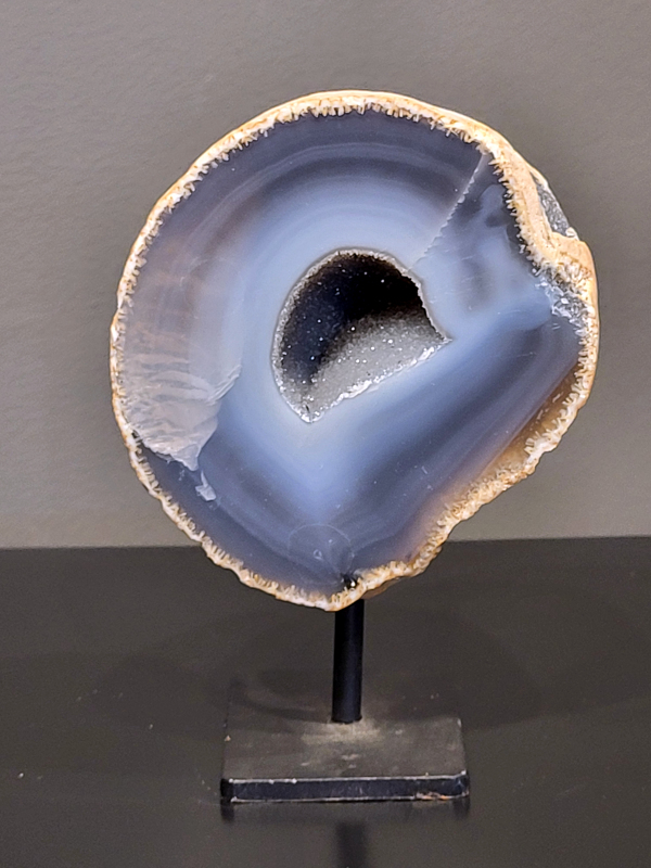 Agaat op standaard, 904 gram, 14cm hg. en 10cm br. 32,- euro, nr. 15
Agaat is een veelzijdige edelsteen die bekend staat om zijn prachtige kleurbanden en patronen. Het is een variëteit van het mineraal kwarts, meer specifiek chalcedoon, en wordt vaak gebruikt in sieraden en als decoratieve steen. 
Algemene kenmerken:
Agaat is een microkristallijne vorm van kwarts, bestaande uit microscopisch kleine kristallen. 
Kleuren en patronen:
Agaat komt voor in vele kleuren, vaak met banden of lagen in verschillende tinten. 
Agaat is een populaire keuze voor het maken van kettingen, armbanden, ringen en andere sieraden vanwege de esthetische aantrekkingskracht en duurzaamheid. 
Spirituele eigenschappen:
Agaat wordt vaak geassocieerd met aardende, stabiliserende en beschermende eigenschappen. 
Helende werking:
Er wordt aangenomen dat agaat kan helpen bij het verminderen van stress, het bevorderen van emotioneel evenwicht en het versterken van het zelfvertrouwen. 
Verzorging van agaat:
Agaat is relatief gemakkelijk te onderhouden. Het kan worden gereinigd met lauw water, de rook van witte salie of palo santo, of door het op een hematiet- of bergkristal-cluster te plaatsen. 

-	Kunstgalerie-Arnold -