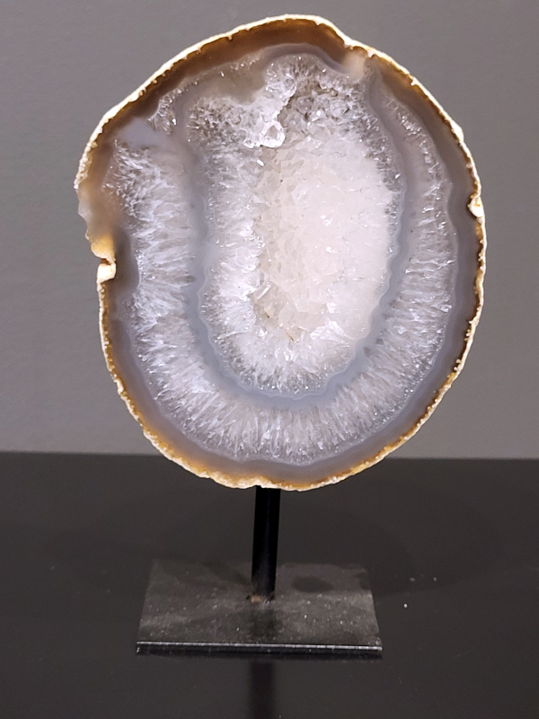 Agaat op standaard, 952 gram, 16cm hg en 10cm br. 33,- euro, nr. 16
Agaat is een veelzijdige edelsteen die bekend staat om zijn prachtige kleurbanden en patronen. Het is een variëteit van het mineraal kwarts, meer specifiek chalcedoon, en wordt vaak gebruikt in sieraden en als decoratieve steen. 
Algemene kenmerken:
Agaat is een microkristallijne vorm van kwarts, bestaande uit microscopisch kleine kristallen. 
Kleuren en patronen:
Agaat komt voor in vele kleuren, vaak met banden of lagen in verschillende tinten. 
Agaat is een populaire keuze voor het maken van kettingen, armbanden, ringen en andere sieraden vanwege de esthetische aantrekkingskracht en duurzaamheid. 
Spirituele eigenschappen:
Agaat wordt vaak geassocieerd met aardende, stabiliserende en beschermende eigenschappen. 
Helende werking:
Er wordt aangenomen dat agaat kan helpen bij het verminderen van stress, het bevorderen van emotioneel evenwicht en het versterken van het zelfvertrouwen. 
Verzorging van agaat:
Agaat is relatief gemakkelijk te onderhouden. Het kan worden gereinigd met lauw water, de rook van witte salie of palo santo, of door het op een hematiet- of bergkristal-cluster te plaatsen. 

-	Kunstgalerie-Arnold -