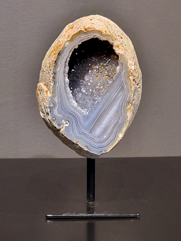 Agaat op standaard, 1,1 kg., 15cm hg. en 8cm br.  37,- euro, nr. 4
Agaat is een veelzijdige edelsteen die bekend staat om zijn prachtige kleurbanden en patronen. Het is een variëteit van het mineraal kwarts, meer specifiek chalcedoon, en wordt vaak gebruikt in sieraden en als decoratieve steen. 
Algemene kenmerken:
Agaat is een microkristallijne vorm van kwarts, bestaande uit microscopisch kleine kristallen. 
Kleuren en patronen:
Agaat komt voor in vele kleuren, vaak met banden of lagen in verschillende tinten. 
Agaat is een populaire keuze voor het maken van kettingen, armbanden, ringen en andere sieraden vanwege de esthetische aantrekkingskracht en duurzaamheid. 
Spirituele eigenschappen:
Agaat wordt vaak geassocieerd met aardende, stabiliserende en beschermende eigenschappen. 
Helende werking:
Er wordt aangenomen dat agaat kan helpen bij het verminderen van stress, het bevorderen van emotioneel evenwicht en het versterken van het zelfvertrouwen. 
Verzorging van agaat:
Agaat is relatief gemakkelijk te onderhouden. Het kan worden gereinigd met lauw water, de rook van witte salie of palo santo, of door het op een hematiet- of bergkristal-cluster te plaatsen. 

-	Kunstgalerie-Arnold -