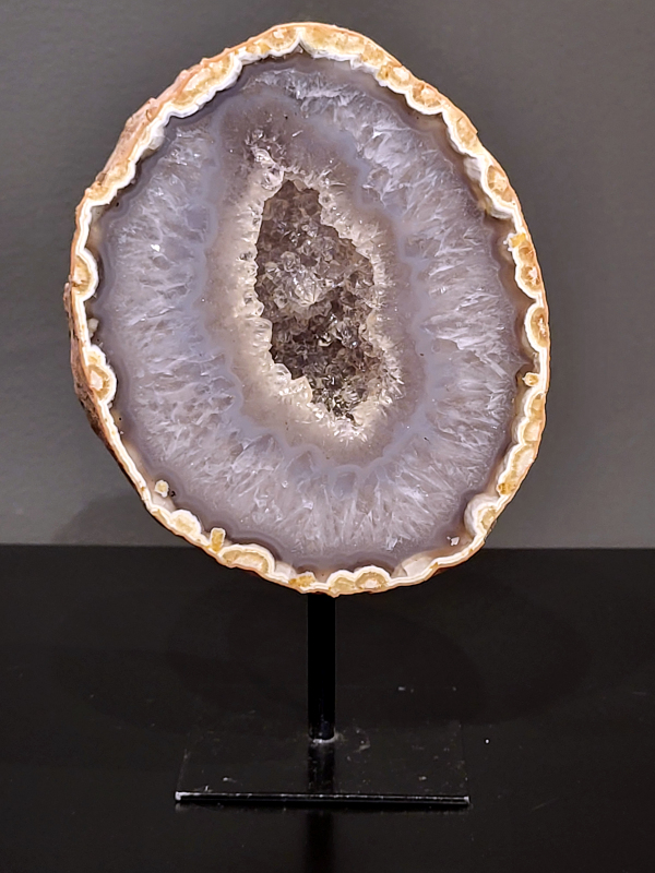 Agaat op standaard, 1,2kg, 17cm hg. en 10cm br. 41,- euro, nr. 6
Agaat is een veelzijdige edelsteen die bekend staat om zijn prachtige kleurbanden en patronen. Het is een variëteit van het mineraal kwarts, meer specifiek chalcedoon, en wordt vaak gebruikt in sieraden en als decoratieve steen. 
Algemene kenmerken:
Agaat is een microkristallijne vorm van kwarts, bestaande uit microscopisch kleine kristallen. 
Kleuren en patronen:
Agaat komt voor in vele kleuren, vaak met banden of lagen in verschillende tinten. 
Agaat is een populaire keuze voor het maken van kettingen, armbanden, ringen en andere sieraden vanwege de esthetische aantrekkingskracht en duurzaamheid. 
Spirituele eigenschappen:
Agaat wordt vaak geassocieerd met aardende, stabiliserende en beschermende eigenschappen. 
Helende werking:
Er wordt aangenomen dat agaat kan helpen bij het verminderen van stress, het bevorderen van emotioneel evenwicht en het versterken van het zelfvertrouwen. 
Verzorging van agaat:
Agaat is relatief gemakkelijk te onderhouden. Het kan worden gereinigd met lauw water, de rook van witte salie of palo santo, of door het op een hematiet- of bergkristal-cluster te plaatsen. 

-	Kunstgalerie-Arnold -