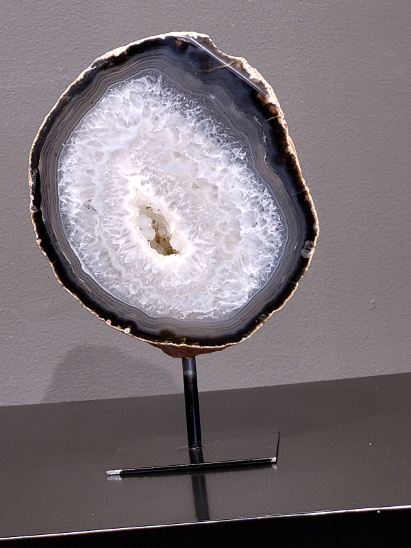 Agaat op standaard, 1,3 kg , 20cm hg. en 13cm br. 45,- euro, nr. 7
Agaat is een veelzijdige edelsteen die bekend staat om zijn prachtige kleurbanden en patronen. Het is een variëteit van het mineraal kwarts, meer specifiek chalcedoon, en wordt vaak gebruikt in sieraden en als decoratieve steen. 
Algemene kenmerken:
Agaat is een microkristallijne vorm van kwarts, bestaande uit microscopisch kleine kristallen. 
Kleuren en patronen:
Agaat komt voor in vele kleuren, vaak met banden of lagen in verschillende tinten. 
Agaat is een populaire keuze voor het maken van kettingen, armbanden, ringen en andere sieraden vanwege de esthetische aantrekkingskracht en duurzaamheid. 
Spirituele eigenschappen:
Agaat wordt vaak geassocieerd met aardende, stabiliserende en beschermende eigenschappen. 
Helende werking:
Er wordt aangenomen dat agaat kan helpen bij het verminderen van stress, het bevorderen van emotioneel evenwicht en het versterken van het zelfvertrouwen. 
Verzorging van agaat:
Agaat is relatief gemakkelijk te onderhouden. Het kan worden gereinigd met lauw water, de rook van witte salie of palo santo, of door het op een hematiet- of bergkristal-cluster te plaatsen. 

-	Kunstgalerie-Arnold -
