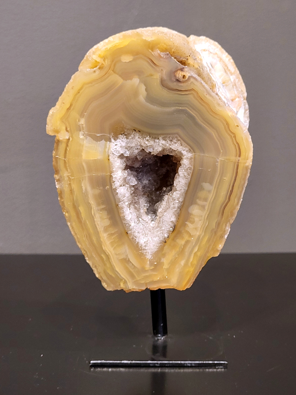 Agaat op standaard, 658 gram, 14cm hg. en 8cm br.  23,- euro, nr. 9
Agaat is een veelzijdige edelsteen die bekend staat om zijn prachtige kleurbanden en patronen. Het is een variëteit van het mineraal kwarts, meer specifiek chalcedoon, en wordt vaak gebruikt in sieraden en als decoratieve steen. 
Algemene kenmerken:
Agaat is een microkristallijne vorm van kwarts, bestaande uit microscopisch kleine kristallen. 
Kleuren en patronen:
Agaat komt voor in vele kleuren, vaak met banden of lagen in verschillende tinten. 
Agaat is een populaire keuze voor het maken van kettingen, armbanden, ringen en andere sieraden vanwege de esthetische aantrekkingskracht en duurzaamheid. 
Spirituele eigenschappen:
Agaat wordt vaak geassocieerd met aardende, stabiliserende en beschermende eigenschappen. 
Helende werking:
Er wordt aangenomen dat agaat kan helpen bij het verminderen van stress, het bevorderen van emotioneel evenwicht en het versterken van het zelfvertrouwen. 
Verzorging van agaat:
Agaat is relatief gemakkelijk te onderhouden. Het kan worden gereinigd met lauw water, de rook van witte salie of palo santo, of door het op een hematiet- of bergkristal-cluster te plaatsen. 

-	Kunstgalerie-Arnold -
