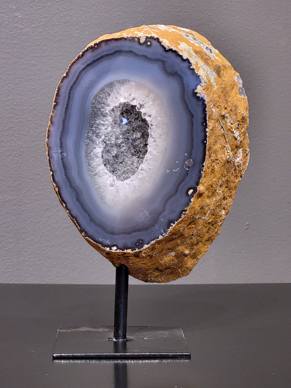 Agaat op standaard, 820 gram, 17cm hg en 11cm br 29,- euro, nr. 10
Agaat is een veelzijdige edelsteen die bekend staat om zijn prachtige kleurbanden en patronen. Het is een variëteit van het mineraal kwarts, meer specifiek chalcedoon, en wordt vaak gebruikt in sieraden en als decoratieve steen. 
Algemene kenmerken:
Agaat is een microkristallijne vorm van kwarts, bestaande uit microscopisch kleine kristallen. 
Kleuren en patronen:
Agaat komt voor in vele kleuren, vaak met banden of lagen in verschillende tinten. 
Agaat is een populaire keuze voor het maken van kettingen, armbanden, ringen en andere sieraden vanwege de esthetische aantrekkingskracht en duurzaamheid. 
Spirituele eigenschappen:
Agaat wordt vaak geassocieerd met aardende, stabiliserende en beschermende eigenschappen. 
Helende werking:
Er wordt aangenomen dat agaat kan helpen bij het verminderen van stress, het bevorderen van emotioneel evenwicht en het versterken van het zelfvertrouwen. 
Verzorging van agaat:
Agaat is relatief gemakkelijk te onderhouden. Het kan worden gereinigd met lauw water, de rook van witte salie of palo santo, of door het op een hematiet- of bergkristal-cluster te plaatsen. 

-	Kunstgalerie-Arnold -
