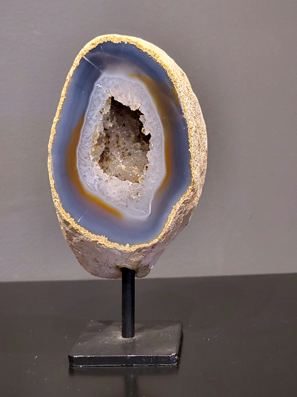 Agaat op standaard, 760 gram, 16cm hg. en 8cm br.  27,- euro, nr. 11
Agaat is een veelzijdige edelsteen die bekend staat om zijn prachtige kleurbanden en patronen. Het is een variëteit van het mineraal kwarts, meer specifiek chalcedoon, en wordt vaak gebruikt in sieraden en als decoratieve steen. 
Algemene kenmerken:
Agaat is een microkristallijne vorm van kwarts, bestaande uit microscopisch kleine kristallen. 
Kleuren en patronen:
Agaat komt voor in vele kleuren, vaak met banden of lagen in verschillende tinten. 
Agaat is een populaire keuze voor het maken van kettingen, armbanden, ringen en andere sieraden vanwege de esthetische aantrekkingskracht en duurzaamheid. 
Spirituele eigenschappen:
Agaat wordt vaak geassocieerd met aardende, stabiliserende en beschermende eigenschappen. 
Helende werking:
Er wordt aangenomen dat agaat kan helpen bij het verminderen van stress, het bevorderen van emotioneel evenwicht en het versterken van het zelfvertrouwen. 
Verzorging van agaat:
Agaat is relatief gemakkelijk te onderhouden. Het kan worden gereinigd met lauw water, de rook van witte salie of palo santo, of door het op een hematiet- of bergkristal-cluster te plaatsen. 

-	Kunstgalerie-Arnold -
