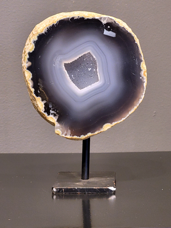 Agaat op standaard, 866 gram, 15cm hg. en 11cm br. 30,- euro, nr. 26
Agaat is een veelzijdige edelsteen die bekend staat om zijn prachtige kleurbanden en patronen. Het is een variëteit van het mineraal kwarts, meer specifiek chalcedoon, en wordt vaak gebruikt in sieraden en als decoratieve steen. 
Algemene kenmerken:
Agaat is een microkristallijne vorm van kwarts, bestaande uit microscopisch kleine kristallen. 
Kleuren en patronen:
Agaat komt voor in vele kleuren, vaak met banden of lagen in verschillende tinten. 
Agaat is een populaire keuze voor het maken van kettingen, armbanden, ringen en andere sieraden vanwege de esthetische aantrekkingskracht en duurzaamheid. 
Spirituele eigenschappen:
Agaat wordt vaak geassocieerd met aardende, stabiliserende en beschermende eigenschappen. 
Helende werking:
Er wordt aangenomen dat agaat kan helpen bij het verminderen van stress, het bevorderen van emotioneel evenwicht en het versterken van het zelfvertrouwen. 
Verzorging van agaat:
Agaat is relatief gemakkelijk te onderhouden. Het kan worden gereinigd met lauw water, de rook van witte salie of palo santo, of door het op een hematiet- of bergkristal-cluster te plaatsen. 

-	Kunstgalerie-Arnold -