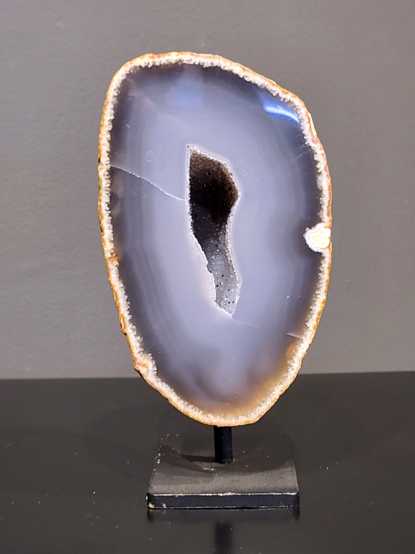 Agaat op standaard, 870 gram, 15cm hg. en 8cm br.  30,- euro, nr. 27
Agaat is een veelzijdige edelsteen die bekend staat om zijn prachtige kleurbanden en patronen. Het is een variëteit van het mineraal kwarts, meer specifiek chalcedoon, en wordt vaak gebruikt in sieraden en als decoratieve steen. 
Algemene kenmerken:
Agaat is een microkristallijne vorm van kwarts, bestaande uit microscopisch kleine kristallen. 
Kleuren en patronen:
Agaat komt voor in vele kleuren, vaak met banden of lagen in verschillende tinten. 
Agaat is een populaire keuze voor het maken van kettingen, armbanden, ringen en andere sieraden vanwege de esthetische aantrekkingskracht en duurzaamheid. 
Spirituele eigenschappen:
Agaat wordt vaak geassocieerd met aardende, stabiliserende en beschermende eigenschappen. 
Helende werking:
Er wordt aangenomen dat agaat kan helpen bij het verminderen van stress, het bevorderen van emotioneel evenwicht en het versterken van het zelfvertrouwen. 
Verzorging van agaat:
Agaat is relatief gemakkelijk te onderhouden. Het kan worden gereinigd met lauw water, de rook van witte salie of palo santo, of door het op een hematiet- of bergkristal-cluster te plaatsen. 

-	Kunstgalerie-Arnold -