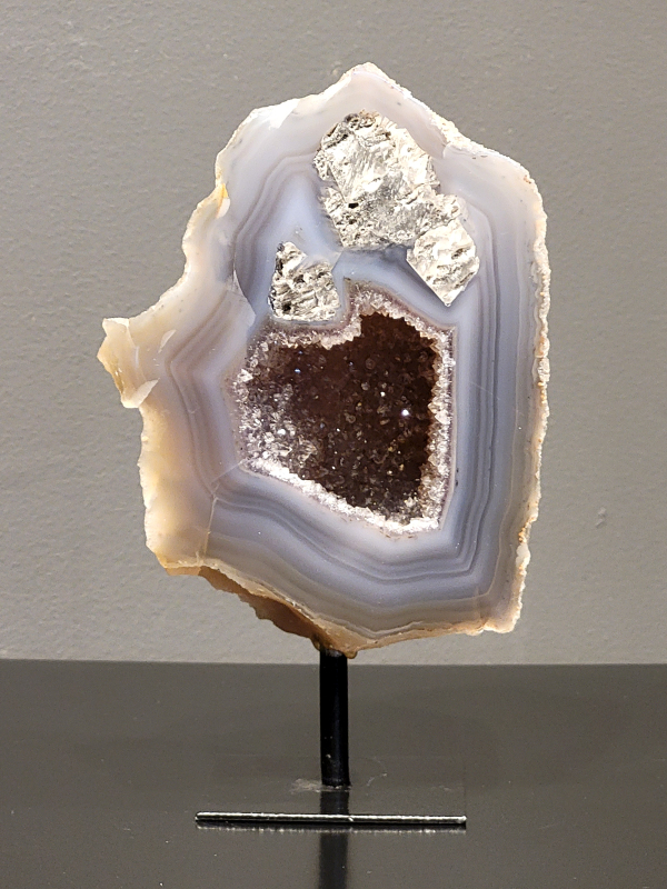 Agaat op standaard, 928 gram, 17cm hoog en 10cm br. 32,- euro, nr. 30
Agaat is een veelzijdige edelsteen die bekend staat om zijn prachtige kleurbanden en patronen. Het is een variëteit van het mineraal kwarts, meer specifiek chalcedoon, en wordt vaak gebruikt in sieraden en als decoratieve steen. 
Algemene kenmerken:
Agaat is een microkristallijne vorm van kwarts, bestaande uit microscopisch kleine kristallen. 
Kleuren en patronen:
Agaat komt voor in vele kleuren, vaak met banden of lagen in verschillende tinten. 
Agaat is een populaire keuze voor het maken van kettingen, armbanden, ringen en andere sieraden vanwege de esthetische aantrekkingskracht en duurzaamheid. 
Spirituele eigenschappen:
Agaat wordt vaak geassocieerd met aardende, stabiliserende en beschermende eigenschappen. 
Helende werking:
Er wordt aangenomen dat agaat kan helpen bij het verminderen van stress, het bevorderen van emotioneel evenwicht en het versterken van het zelfvertrouwen. 
Verzorging van agaat:
Agaat is relatief gemakkelijk te onderhouden. Het kan worden gereinigd met lauw water, de rook van witte salie of palo santo, of door het op een hematiet- of bergkristal-cluster te plaatsen. 

-	Kunstgalerie-Arnold -