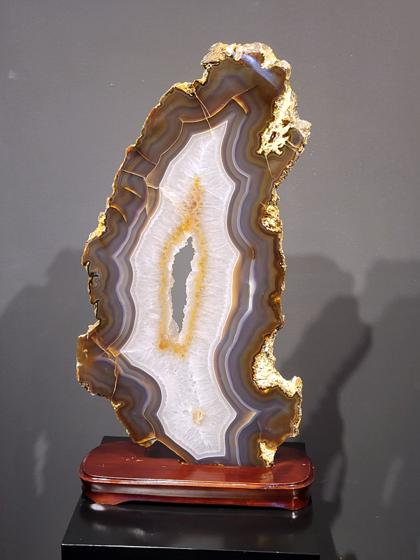 Agaat op standaard, 4,3kg, 60cm hg en 30cm br. 225,- euro, nr. 31
Agaat is een veelzijdige edelsteen die bekend staat om zijn prachtige kleurbanden en patronen. Het is een variëteit van het mineraal kwarts, meer specifiek chalcedoon, en wordt vaak gebruikt in sieraden en als decoratieve steen. 
Algemene kenmerken:
Agaat is een microkristallijne vorm van kwarts, bestaande uit microscopisch kleine kristallen. 
Kleuren en patronen:
Agaat komt voor in vele kleuren, vaak met banden of lagen in verschillende tinten. 
Agaat is een populaire keuze voor het maken van kettingen, armbanden, ringen en andere sieraden vanwege de esthetische aantrekkingskracht en duurzaamheid. 
Spirituele eigenschappen:
Agaat wordt vaak geassocieerd met aardende, stabiliserende en beschermende eigenschappen. 
Helende werking:
Er wordt aangenomen dat agaat kan helpen bij het verminderen van stress, het bevorderen van emotioneel evenwicht en het versterken van het zelfvertrouwen. 
Verzorging van agaat:
Agaat is relatief gemakkelijk te onderhouden. Het kan worden gereinigd met lauw water, de rook van witte salie of palo santo, of door het op een hematiet- of bergkristal-cluster te plaatsen. 

-	Kunstgalerie-Arnold -