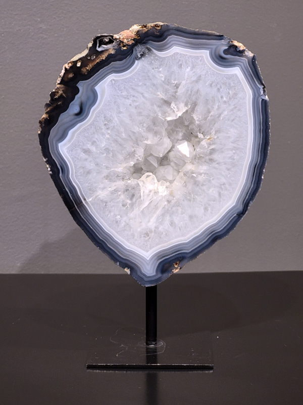 Agaat op standaard, 1,4kg., 19cm hg. en 13cm br. 50,- euro, nr. 18
Agaat is een veelzijdige edelsteen die bekend staat om zijn prachtige kleurbanden en patronen. Het is een variëteit van het mineraal kwarts, meer specifiek chalcedoon, en wordt vaak gebruikt in sieraden en als decoratieve steen. 
Algemene kenmerken:
Agaat is een microkristallijne vorm van kwarts, bestaande uit microscopisch kleine kristallen. 
Kleuren en patronen:
Agaat komt voor in vele kleuren, vaak met banden of lagen in verschillende tinten. 
Agaat is een populaire keuze voor het maken van kettingen, armbanden, ringen en andere sieraden vanwege de esthetische aantrekkingskracht en duurzaamheid. 
Spirituele eigenschappen:
Agaat wordt vaak geassocieerd met aardende, stabiliserende en beschermende eigenschappen. 
Helende werking:
Er wordt aangenomen dat agaat kan helpen bij het verminderen van stress, het bevorderen van emotioneel evenwicht en het versterken van het zelfvertrouwen. 
Verzorging van agaat:
Agaat is relatief gemakkelijk te onderhouden. Het kan worden gereinigd met lauw water, de rook van witte salie of palo santo, of door het op een hematiet- of bergkristal-cluster te plaatsen. 

-	Kunstgalerie-Arnold -