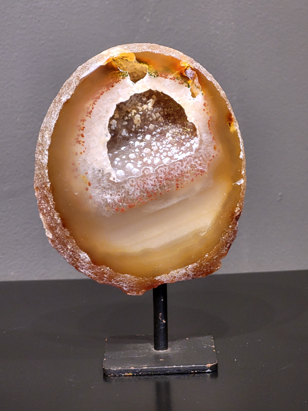 Agaat op standaard, 516 gram, 15cm hg. en 10cm br. 18,- euro, nr. 19
Agaat is een veelzijdige edelsteen die bekend staat om zijn prachtige kleurbanden en patronen. Het is een variëteit van het mineraal kwarts, meer specifiek chalcedoon, en wordt vaak gebruikt in sieraden en als decoratieve steen. 
Algemene kenmerken:
Agaat is een microkristallijne vorm van kwarts, bestaande uit microscopisch kleine kristallen. 
Kleuren en patronen:
Agaat komt voor in vele kleuren, vaak met banden of lagen in verschillende tinten. 
Agaat is een populaire keuze voor het maken van kettingen, armbanden, ringen en andere sieraden vanwege de esthetische aantrekkingskracht en duurzaamheid. 
Spirituele eigenschappen:
Agaat wordt vaak geassocieerd met aardende, stabiliserende en beschermende eigenschappen. 
Helende werking:
Er wordt aangenomen dat agaat kan helpen bij het verminderen van stress, het bevorderen van emotioneel evenwicht en het versterken van het zelfvertrouwen. 
Verzorging van agaat:
Agaat is relatief gemakkelijk te onderhouden. Het kan worden gereinigd met lauw water, de rook van witte salie of palo santo, of door het op een hematiet- of bergkristal-cluster te plaatsen. 

-	Kunstgalerie-Arnold -
