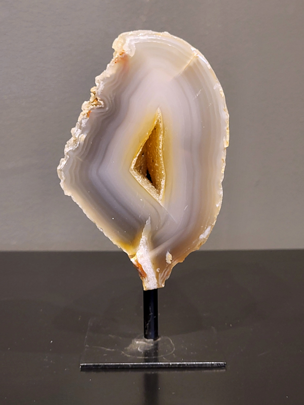 Agaat op standaard, 588 gram, 14cm hg. en 7cm br.  21,- euro, nr. 20
Agaat is een veelzijdige edelsteen die bekend staat om zijn prachtige kleurbanden en patronen. Het is een variëteit van het mineraal kwarts, meer specifiek chalcedoon, en wordt vaak gebruikt in sieraden en als decoratieve steen. 
Algemene kenmerken:
Agaat is een microkristallijne vorm van kwarts, bestaande uit microscopisch kleine kristallen. 
Kleuren en patronen:
Agaat komt voor in vele kleuren, vaak met banden of lagen in verschillende tinten. 
Agaat is een populaire keuze voor het maken van kettingen, armbanden, ringen en andere sieraden vanwege de esthetische aantrekkingskracht en duurzaamheid. 
Spirituele eigenschappen:
Agaat wordt vaak geassocieerd met aardende, stabiliserende en beschermende eigenschappen. 
Helende werking:
Er wordt aangenomen dat agaat kan helpen bij het verminderen van stress, het bevorderen van emotioneel evenwicht en het versterken van het zelfvertrouwen. 
Verzorging van agaat:
Agaat is relatief gemakkelijk te onderhouden. Het kan worden gereinigd met lauw water, de rook van witte salie of palo santo, of door het op een hematiet- of bergkristal-cluster te plaatsen. 

-	Kunstgalerie-Arnold -