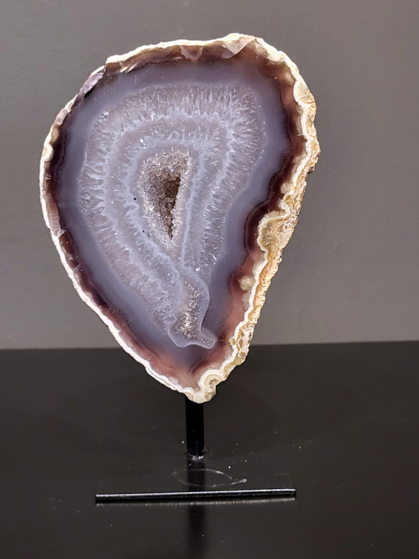 Agaat op standaard, 750 gram, 15cm hg. en 9cm br. 26,- euro, nr. 23
Agaat is een veelzijdige edelsteen die bekend staat om zijn prachtige kleurbanden en patronen. Het is een variëteit van het mineraal kwarts, meer specifiek chalcedoon, en wordt vaak gebruikt in sieraden en als decoratieve steen. 
Algemene kenmerken:
Agaat is een microkristallijne vorm van kwarts, bestaande uit microscopisch kleine kristallen. 
Kleuren en patronen:
Agaat komt voor in vele kleuren, vaak met banden of lagen in verschillende tinten. 
Agaat is een populaire keuze voor het maken van kettingen, armbanden, ringen en andere sieraden vanwege de esthetische aantrekkingskracht en duurzaamheid. 
Spirituele eigenschappen:
Agaat wordt vaak geassocieerd met aardende, stabiliserende en beschermende eigenschappen. 
Helende werking:
Er wordt aangenomen dat agaat kan helpen bij het verminderen van stress, het bevorderen van emotioneel evenwicht en het versterken van het zelfvertrouwen. 
Verzorging van agaat:
Agaat is relatief gemakkelijk te onderhouden. Het kan worden gereinigd met lauw water, de rook van witte salie of palo santo, of door het op een hematiet- of bergkristal-cluster te plaatsen. 

-	Kunstgalerie-Arnold -