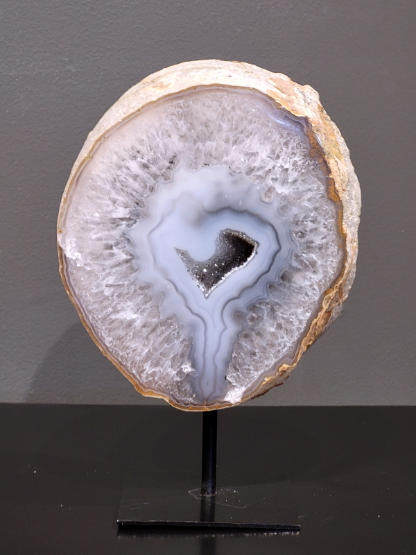 Agaat op standaard, 1,4 kg., 19cm hg. en 13cm br. 48,- euro, nr. 2
Agaat is een veelzijdige edelsteen die bekend staat om zijn prachtige kleurbanden en patronen. Het is een variëteit van het mineraal kwarts, meer specifiek chalcedoon, en wordt vaak gebruikt in sieraden en als decoratieve steen. 
Algemene kenmerken:
Agaat is een microkristallijne vorm van kwarts, bestaande uit microscopisch kleine kristallen. 
Kleuren en patronen:
Agaat komt voor in vele kleuren, vaak met banden of lagen in verschillende tinten. 
Agaat is een populaire keuze voor het maken van kettingen, armbanden, ringen en andere sieraden vanwege de esthetische aantrekkingskracht en duurzaamheid. 
Spirituele eigenschappen:
Agaat wordt vaak geassocieerd met aardende, stabiliserende en beschermende eigenschappen. 
Helende werking:
Er wordt aangenomen dat agaat kan helpen bij het verminderen van stress, het bevorderen van emotioneel evenwicht en het versterken van het zelfvertrouwen. 
Verzorging van agaat:
Agaat is relatief gemakkelijk te onderhouden. Het kan worden gereinigd met lauw water, de rook van witte salie of palo santo, of door het op een hematiet- of bergkristal-cluster te plaatsen. 

-Kunstgalerie-Arnold -