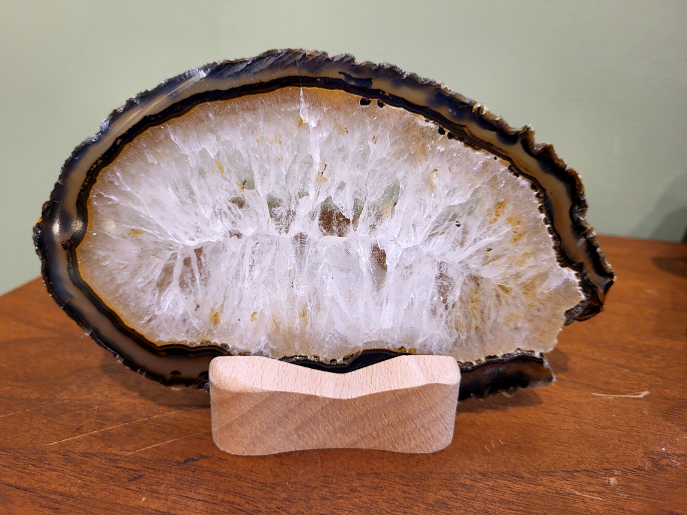 Agaatschijf, waxinelicht,17cm breed, 22,- euro, nr. 42
Beschrijving Agaat.

Agaat is een veelzijdige edelsteen die bekend staat om zijn prachtige kleurbanden en patronen. Het is een variëteit van het mineraal kwarts, meer specifiek chalcedoon, en wordt vaak gebruikt in sieraden en als decoratieve steen. 
Algemene kenmerken:
Samenstelling:
Agaat is een microkristallijne vorm van kwarts, bestaande uit microscopisch kleine kristallen. 
Kleuren en patronen:
Agaat komt voor in vele kleuren, vaak met banden of lagen in verschillende tinten. 
Hardheid:
Agaat heeft een hardheid van 6,5 tot 7 op de schaal van Mohs, wat betekent dat het een relatief duurzame steen is. 
Herkomst:
De naam "agaat" is afgeleid van de rivier Achates (nu Drillo) op Sicilië, waar de steen voor het eerst werd ontdekt. 
Eigenschappen en toepassingen:
Sieraden:
Agaat is een populaire keuze voor het maken van kettingen, armbanden, ringen en andere sieraden vanwege de esthetische aantrekkingskracht en duurzaamheid. 
Spirituele eigenschappen:
Agaat wordt vaak geassocieerd met aardende, stabiliserende en beschermende eigenschappen. 
Helende werking:
Er wordt aangenomen dat agaat kan helpen bij het verminderen van stress, het bevorderen van emotioneel evenwicht en het versterken van het zelfvertrouwen. 
Andere toepassingen:
Agaat wordt ook gebruikt in decoratieve objecten, zoals schijven en tafels, en werd in het verleden gebruikt in oude culturen voor bescherming en geluk. 
Soorten agaat:
Er zijn veel verschillende soorten agaat, elk met hun eigen unieke kenmerken en eigenschappen, zoals:
Botswana agaat: Bekend om zijn zachte, kalmerende energie en kan helpen bij het loslaten van negatieve emoties. 
Witte agaat: Vaak geassocieerd met innerlijke rust en evenwicht. 
Grijze agaat: Kan helpen bij het stellen van orde en het vinden van stabiliteit. 
Agaat geode: Kan rustgevend werken en chaos tegengaan. 
Verzorging van agaat:
Agaat is relatief gemakkelijk te onderhouden. Het kan worden gereinigd met lauw water, de rook van witte salie of palo santo, of door het op een hematiet- of bergkristal-cluster te plaatsen.