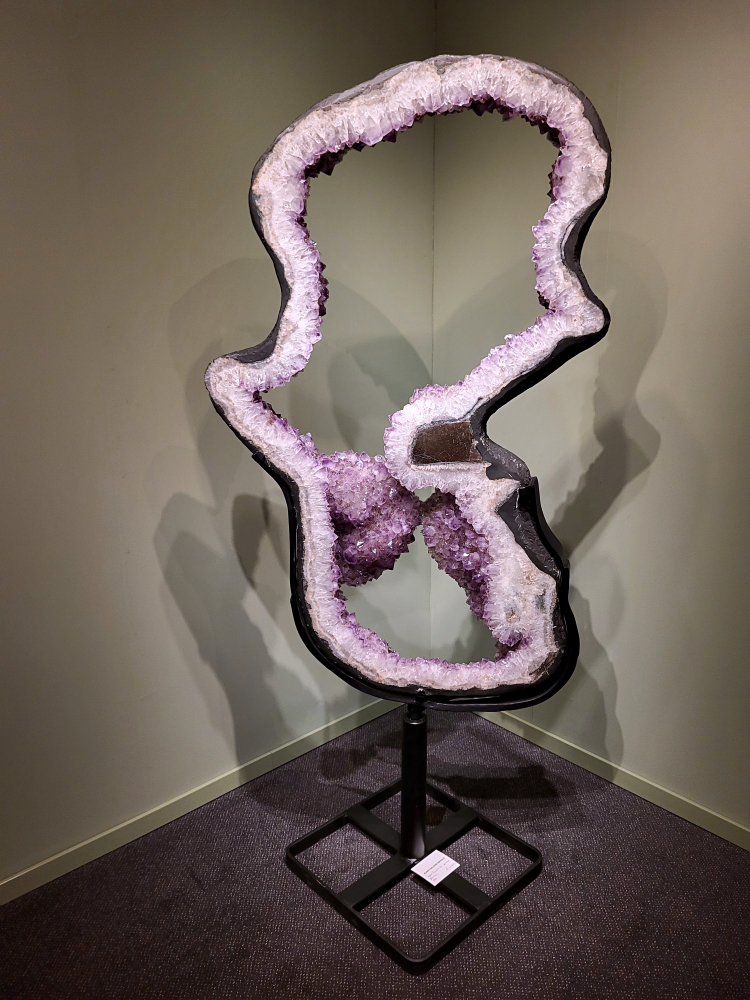 Amethist, 1.80 hoog, 80 kg op standaard, topstuk, 4500,- euro, nr. 44

Amethist is een paarse variëteit van kwarts, bekend om zijn kalmerende en spirituele eigenschappen. De kleur varieert van licht lila tot diep violet en wordt veroorzaakt door sporen van ijzer en andere elementen. Amethist wordt al eeuwenlang gewaardeerd, zowel vanwege zijn esthetische schoonheid als zijn vermeende genezende en beschermende krachten. 
Amethist is een kwartskristal, vaak te vinden in geodes (holtes in gesteente) of als afzonderlijke kristallen. 
De kleur varieert van lichtpaars tot diep violet, soms met roze of blauwe tinten. 
De kleurintensiteit kan variëren, waarbij donkerdere amethisten vaak als kwalitatief worden beschouwd. 
Soms vertoont amethist dichroïsme, waarbij je verschillende kleuren kunt zien wanneer je de steen in het licht draait. 

Vindplaatsen:
Amethist wordt gevonden in verschillende delen van de wereld, waaronder Brazilië, Uruguay, Zambia, Madagaskar, Rusland en Canada.
Het wordt vaak gevonden in bergachtige gebieden. 

Gebruik:
Amethist wordt gebruikt in sieraden, decoratieve objecten en als helende steen. 
Het wordt vaak gedragen als hanger, ring of armband, of geplaatst in ruimtes om de energie te zuiveren. 
Amethist wordt ook gebruikt in meditatie en andere spirituele praktijken.