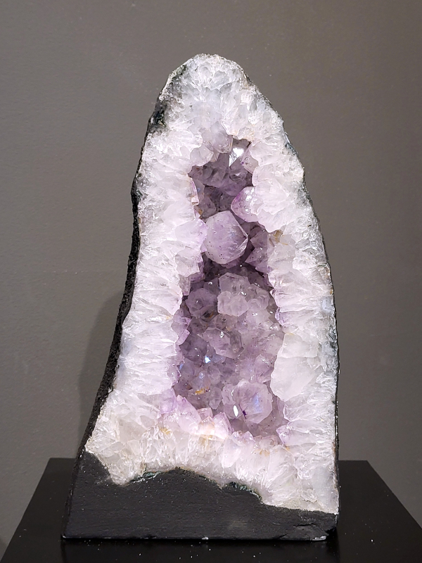 Amethist, 10,3 kg., 35cm hg. en 20cm br. 180,- euro, nr. 58
Beschrijving Amethist.
Amethist is een paarse variëteit van kwarts, bekend om zijn kalmerende en spirituele eigenschappen. De kleur varieert van licht lila tot diep violet en wordt veroorzaakt door sporen van ijzer en andere elementen. Amethist wordt al eeuwenlang gewaardeerd, zowel vanwege zijn esthetische schoonheid als zijn vermeende genezende en beschermende krachten. 
Amethist is een kwartskristal, vaak te vinden in geodes (holtes in gesteente) of als afzonderlijke kristallen. 
De kleur varieert van lichtpaars tot diep violet, soms met roze of blauwe tinten. 
De kleurintensiteit kan variëren, waarbij donkerdere amethisten vaak als kwalitatief worden beschouwd. 
Soms vertoont amethist dichroïsme, waarbij je verschillende kleuren kunt zien wanneer je de steen in het licht draait. 

Vindplaatsen:
Amethist wordt gevonden in verschillende delen van de wereld, waaronder Brazilië, Uruguay, Zambia, Madagaskar, Rusland en Canada.
Het wordt vaak gevonden in bergachtige gebieden. 

Gebruik:
Amethist wordt gebruikt in sieraden, decoratieve objecten en als helende steen. 
Het wordt vaak gedragen als hanger, ring of armband, of geplaatst in ruimtes om de energie te zuiveren. 
Amethist wordt ook gebruikt in meditatie en andere spirituele praktijken.