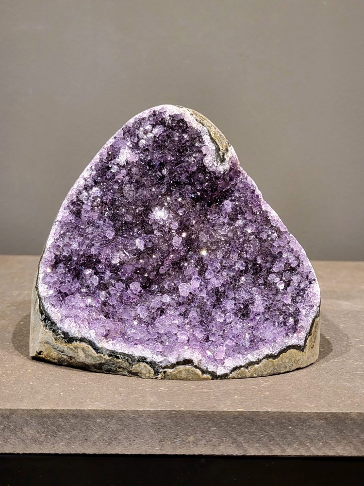 Amethist druzy, 0,9kg, 40,- euro, nr. 33

Beschrijving Amethist.
Amethist is een paarse variëteit van kwarts, bekend om zijn kalmerende en spirituele eigenschappen. De kleur varieert van licht lila tot diep violet en wordt veroorzaakt door sporen van ijzer en andere elementen. Amethist wordt al eeuwenlang gewaardeerd, zowel vanwege zijn esthetische schoonheid als zijn vermeende genezende en beschermende krachten. 
Amethist is een kwartskristal, vaak te vinden in geodes (holtes in gesteente) of als afzonderlijke kristallen. 
De kleur varieert van lichtpaars tot diep violet, soms met roze of blauwe tinten. 
De kleurintensiteit kan variëren, waarbij donkerdere amethisten vaak als kwalitatief worden beschouwd. 
Soms vertoont amethist dichroïsme, waarbij je verschillende kleuren kunt zien wanneer je de steen in het licht draait. 

Vindplaatsen:
Amethist wordt gevonden in verschillende delen van de wereld, waaronder Brazilië, Uruguay, Zambia, Madagaskar, Rusland en Canada.
Het wordt vaak gevonden in bergachtige gebieden. 

Gebruik:
Amethist wordt gebruikt in sieraden, decoratieve objecten en als helende steen. 
Het wordt vaak gedragen als hanger, ring of armband, of geplaatst in ruimtes om de energie te zuiveren. 
Amethist wordt ook gebruikt in meditatie en andere spirituele praktijken. 