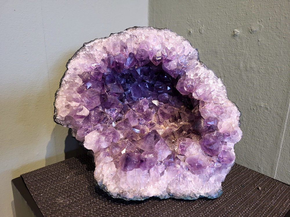 Amethist Cluster Geode, 9,7 kg, 27 cm breed en 22cm diep, 270,- euro, nr.10

Waar komt amethist vandaan en hoe ontstaan ze?
Amethist wordt wereldwijd gevonden maar de grootste
vondsten worden gedaan in Brazilië, Uruguay, Mexico en Zambia.
Deze edelsteen komt voor in basalt holtes of geodes die ontstaan zijn door
vulkaanuitbarstingen, het duurt miljoenen jaren voordat de kristallen zich vormen.
De kleur van de amethist wordt veroorzaakt door de aanwezigheid
van ijzer en mangaan. 
Waar kan amethist niet goed tegen?
Amethist kan niet goed tegen fel zonlicht en plotselinge
temperatuurwisselingen. Langdurige blootstelling aan zonlicht
doet de kleur doen vervagen en abrupte temperatuur veranderingen
kan voor barsten en/of scheuren zorgen. Amethist kan daarentegen
wel grotendeels tegen water.
Spirituele werking van de amethist:
> Rust, spirituele groei en bescherming.
Amethist staat vooral bekend om zijn kalmerende werking.

                                                                                        -  Kunstgalerie Arnold  - 