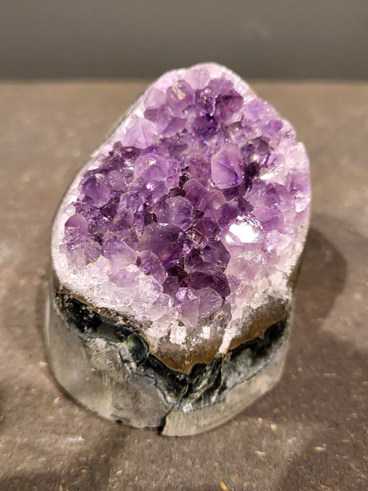 Amethist druzy, 0,4kg, 16,- euro, nr. 14

Beschrijving Amethist.
Amethist is een paarse variëteit van kwarts, bekend om zijn kalmerende en spirituele eigenschappen. De kleur varieert van licht lila tot diep violet en wordt veroorzaakt door sporen van ijzer en andere elementen. Amethist wordt al eeuwenlang gewaardeerd, zowel vanwege zijn esthetische schoonheid als zijn vermeende genezende en beschermende krachten. 
Amethist is een kwartskristal, vaak te vinden in geodes (holtes in gesteente) of als afzonderlijke kristallen. 
De kleur varieert van lichtpaars tot diep violet, soms met roze of blauwe tinten. 
De kleurintensiteit kan variëren, waarbij donkerdere amethisten vaak als kwalitatief worden beschouwd. 
Soms vertoont amethist dichroïsme, waarbij je verschillende kleuren kunt zien wanneer je de steen in het licht draait. 

Vindplaatsen:
Amethist wordt gevonden in verschillende delen van de wereld, waaronder Brazilië, Uruguay, Zambia, Madagaskar, Rusland en Canada.
Het wordt vaak gevonden in bergachtige gebieden. 

Gebruik:
Amethist wordt gebruikt in sieraden, decoratieve objecten en als helende steen. 
Het wordt vaak gedragen als hanger, ring of armband, of geplaatst in ruimtes om de energie te zuiveren. 
Amethist wordt ook gebruikt in meditatie en andere spirituele praktijken. 