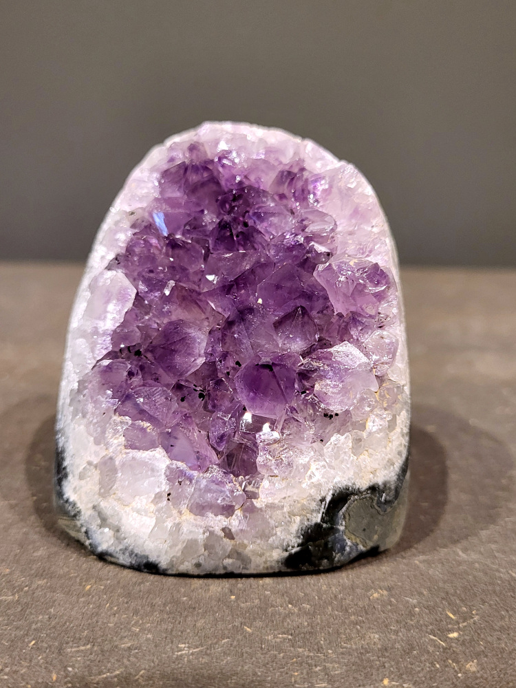 Amethist druzy, 0,4 kg, 18,- euro, nr. 13

Beschrijving Amethist.
Amethist is een paarse variëteit van kwarts, bekend om zijn kalmerende en spirituele eigenschappen. De kleur varieert van licht lila tot diep violet en wordt veroorzaakt door sporen van ijzer en andere elementen. Amethist wordt al eeuwenlang gewaardeerd, zowel vanwege zijn esthetische schoonheid als zijn vermeende genezende en beschermende krachten. 
Amethist is een kwartskristal, vaak te vinden in geodes (holtes in gesteente) of als afzonderlijke kristallen. 
De kleur varieert van lichtpaars tot diep violet, soms met roze of blauwe tinten. 
De kleurintensiteit kan variëren, waarbij donkerdere amethisten vaak als kwalitatief worden beschouwd. 
Soms vertoont amethist dichroïsme, waarbij je verschillende kleuren kunt zien wanneer je de steen in het licht draait. 

Vindplaatsen:

Amethist wordt gevonden in verschillende delen van de wereld, waaronder Brazilië, Uruguay, Zambia, Madagaskar, Rusland en Canada.
Het wordt vaak gevonden in bergachtige gebieden. 

Gebruik:
Amethist wordt gebruikt in sieraden, decoratieve objecten en als helende steen. 
Het wordt vaak gedragen als hanger, ring of armband, of geplaatst in ruimtes om de energie te zuiveren. 
Amethist wordt ook gebruikt in meditatie en andere spirituele praktijken. 