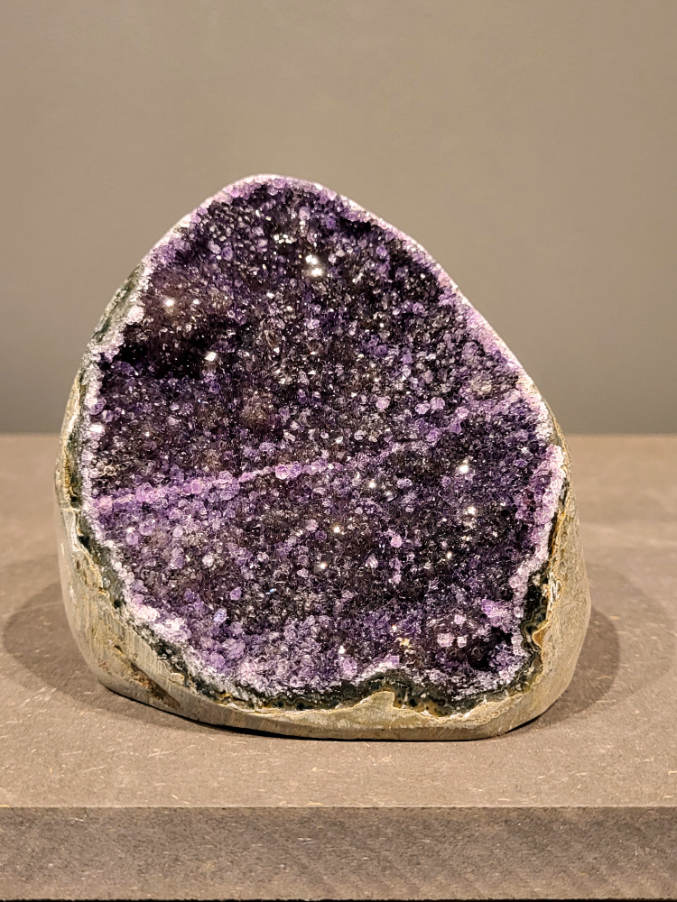 Amethist druzy, 0,7kg, 33,- euro, nr. 19

Beschrijving Amethist.
Amethist is een paarse variëteit van kwarts, bekend om zijn kalmerende en spirituele eigenschappen. De kleur varieert van licht lila tot diep violet en wordt veroorzaakt door sporen van ijzer en andere elementen. Amethist wordt al eeuwenlang gewaardeerd, zowel vanwege zijn esthetische schoonheid als zijn vermeende genezende en beschermende krachten. 
Amethist is een kwartskristal, vaak te vinden in geodes (holtes in gesteente) of als afzonderlijke kristallen. 
De kleur varieert van lichtpaars tot diep violet, soms met roze of blauwe tinten. 
De kleurintensiteit kan variëren, waarbij donkerdere amethisten vaak als kwalitatief worden beschouwd. 
Soms vertoont amethist dichroïsme, waarbij je verschillende kleuren kunt zien wanneer je de steen in het licht draait. 

Vindplaatsen:
Amethist wordt gevonden in verschillende delen van de wereld, waaronder Brazilië, Uruguay, Zambia, Madagaskar, Rusland en Canada.
Het wordt vaak gevonden in bergachtige gebieden. 

Gebruik:
Amethist wordt gebruikt in sieraden, decoratieve objecten en als helende steen. 
Het wordt vaak gedragen als hanger, ring of armband, of geplaatst in ruimtes om de energie te zuiveren. 
Amethist wordt ook gebruikt in meditatie en andere spirituele praktijken. 