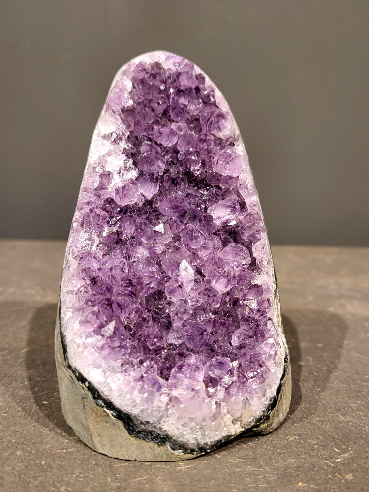 Amethist druzy, 0,7kg, 29,- euro, nr. 30

Beschrijving Amethist.
Amethist is een paarse variëteit van kwarts, bekend om zijn kalmerende en spirituele eigenschappen. De kleur varieert van licht lila tot diep violet en wordt veroorzaakt door sporen van ijzer en andere elementen. Amethist wordt al eeuwenlang gewaardeerd, zowel vanwege zijn esthetische schoonheid als zijn vermeende genezende en beschermende krachten. 
Amethist is een kwartskristal, vaak te vinden in geodes (holtes in gesteente) of als afzonderlijke kristallen. 
De kleur varieert van lichtpaars tot diep violet, soms met roze of blauwe tinten. 
De kleurintensiteit kan variëren, waarbij donkerdere amethisten vaak als kwalitatief worden beschouwd. 
Soms vertoont amethist dichroïsme, waarbij je verschillende kleuren kunt zien wanneer je de steen in het licht draait. 

Vindplaatsen:
Amethist wordt gevonden in verschillende delen van de wereld, waaronder Brazilië, Uruguay, Zambia, Madagaskar, Rusland en Canada.
Het wordt vaak gevonden in bergachtige gebieden. 

Gebruik:
Amethist wordt gebruikt in sieraden, decoratieve objecten en als helende steen. 
Het wordt vaak gedragen als hanger, ring of armband, of geplaatst in ruimtes om de energie te zuiveren. 
Amethist wordt ook gebruikt in meditatie en andere spirituele praktijken. 
