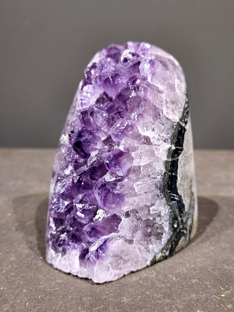 Amethist druzy, 0,7kg, 32,- euro, nr. 18

Beschrijving Amethist.
Amethist is een paarse variëteit van kwarts, bekend om zijn kalmerende en spirituele eigenschappen. De kleur varieert van licht lila tot diep violet en wordt veroorzaakt door sporen van ijzer en andere elementen. Amethist wordt al eeuwenlang gewaardeerd, zowel vanwege zijn esthetische schoonheid als zijn vermeende genezende en beschermende krachten. 
Amethist is een kwartskristal, vaak te vinden in geodes (holtes in gesteente) of als afzonderlijke kristallen. 
De kleur varieert van lichtpaars tot diep violet, soms met roze of blauwe tinten. 
De kleurintensiteit kan variëren, waarbij donkerdere amethisten vaak als kwalitatief worden beschouwd. 
Soms vertoont amethist dichroïsme, waarbij je verschillende kleuren kunt zien wanneer je de steen in het licht draait. 

Vindplaatsen:
Amethist wordt gevonden in verschillende delen van de wereld, waaronder Brazilië, Uruguay, Zambia, Madagaskar, Rusland en Canada.
Het wordt vaak gevonden in bergachtige gebieden. 

Gebruik:
Amethist wordt gebruikt in sieraden, decoratieve objecten en als helende steen. 
Het wordt vaak gedragen als hanger, ring of armband, of geplaatst in ruimtes om de energie te zuiveren. 
Amethist wordt ook gebruikt in meditatie en andere spirituele praktijken. 