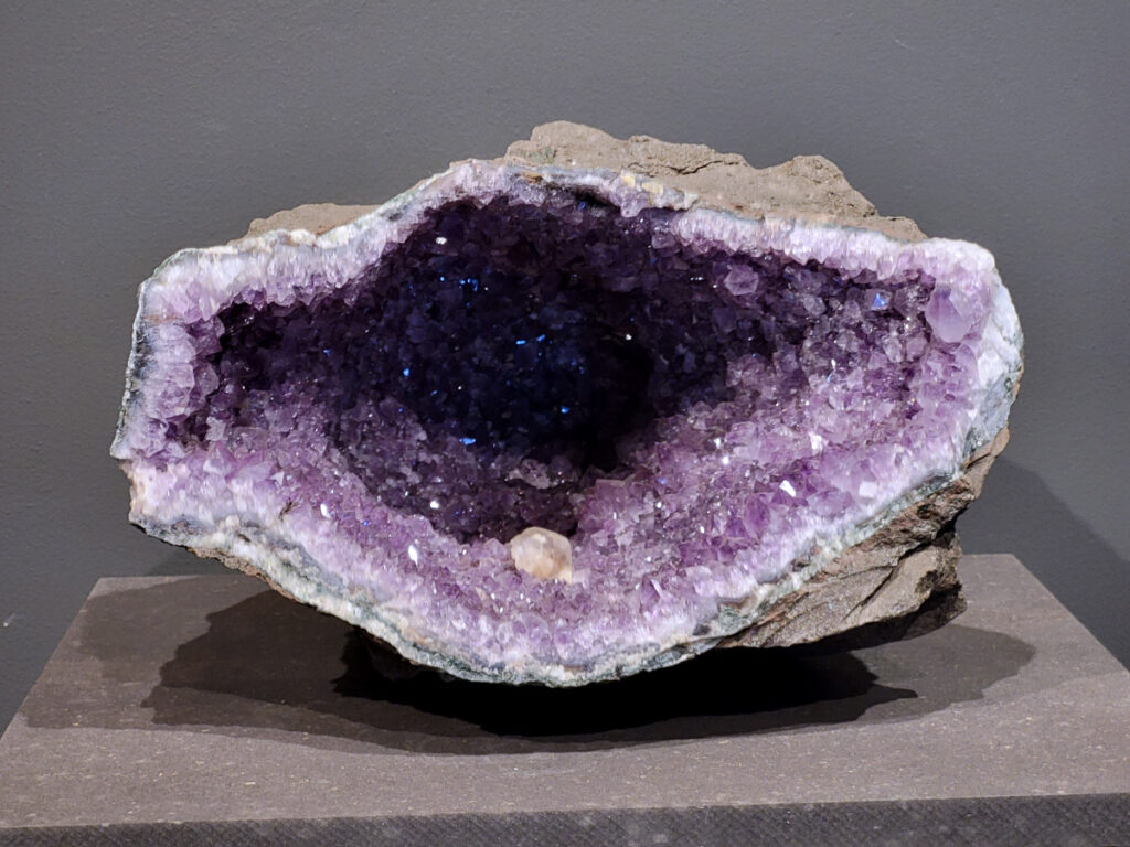 Amethist, 9,2 kg, 248,- euro, nr. 12
Waar komt amethist vandaan en hoe ontstaan ze?
Amethist wordt wereldwijd gevonden maar de grootste
vondsten worden gedaan in Brazilië, Uruguay, Mexico en Zambia.
Deze edelsteen komt voor in basalt holtes of geodes die ontstaan zijn door
vulkaanuitbarstingen, het duurt miljoenen jaren voordat de kristallen zich vormen.
De kleur van de amethist wordt veroorzaakt door de aanwezigheid
van ijzer en mangaan. 
Waar kan amethist niet goed tegen?
Amethist kan niet goed tegen fel zonlicht en plotselinge
temperatuurwisselingen. Langdurige blootstelling aan zonlicht
doet de kleur doen vervagen en abrupte temperatuur veranderingen
kan voor barsten en/of scheuren zorgen. Amethist kan daarentegen
wel grotendeels tegen water.
Spirituele werking van de amethist:
> Rust, spirituele groei en bescherming.
Amethist staat vooral bekend om zijn kalmerende werking.

                                                                                        -  Kunstgalerie Arnold  - 