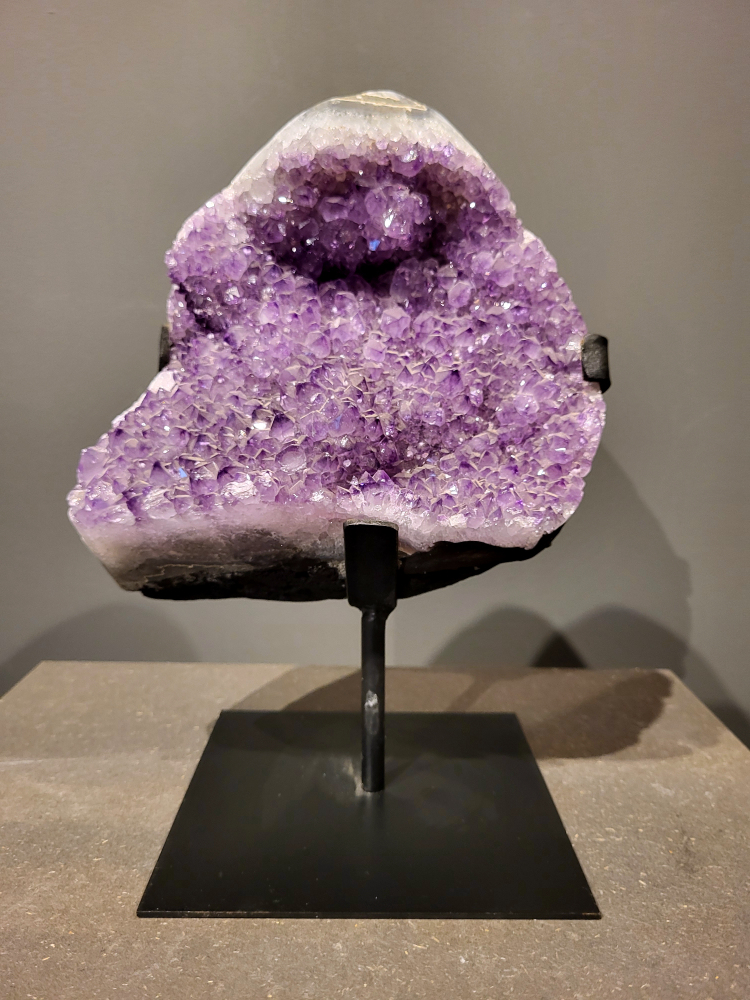 Amethist op standaard, 6,7 kg, 200,- euro, nr. 39
 
Waar komt amethist vandaan en hoe ontstaan ze?
Amethist wordt wereldwijd gevonden maar de grootste
vondsten worden gedaan in Brazilië, Uruguay, Mexico en Zambia.
Deze edelsteen komt voor in basalt holtes of geodes die ontstaan zijn door
vulkaanuitbarstingen, het duurt miljoenen jaren voordat de kristallen zich vormen.
De kleur van de amethist wordt veroorzaakt door de aanwezigheid
van ijzer en mangaan. 
Waar kan amethist niet goed tegen?
Amethist kan niet goed tegen fel zonlicht en plotselinge
temperatuurwisselingen. Langdurige blootstelling aan zonlicht
doet de kleur doen vervagen en abrupte temperatuur veranderingen
kan voor barsten en/of scheuren zorgen. Amethist kan daarentegen
wel grotendeels tegen water.
Spirituele werking van de amethist:
> Rust, spirituele groei en bescherming.
Amethist staat vooral bekend om zijn kalmerende werking.

                                                                                        -  Kunstgalerie Arnold  - 
