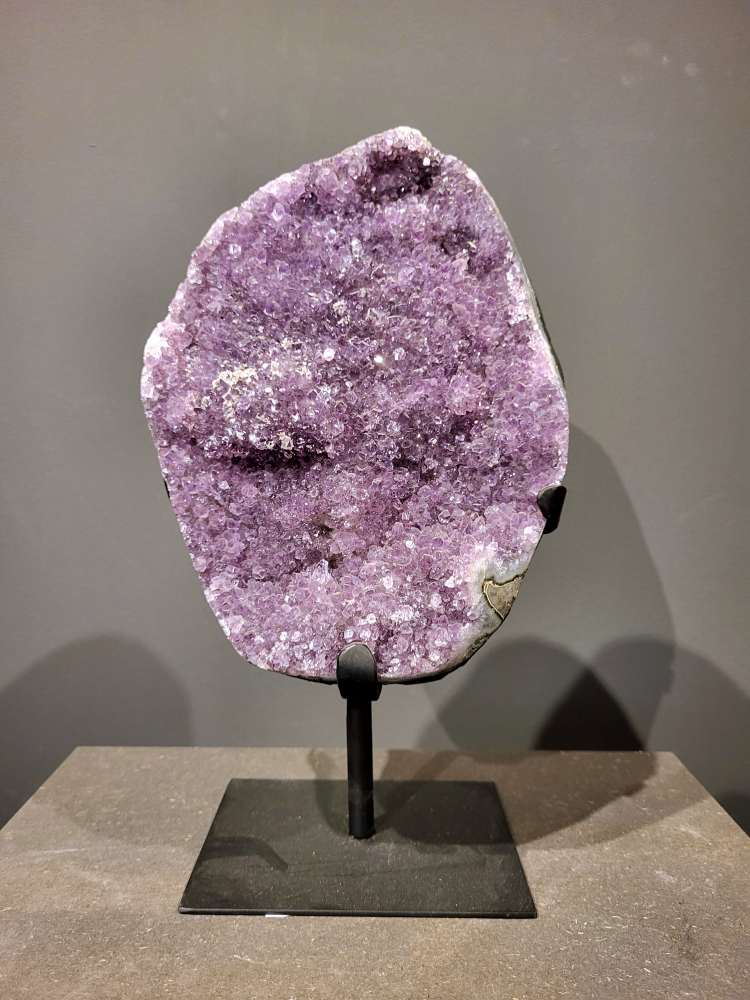 Amethist op standaard, 6,2 kg, 185,- euro, nr. 43
Waar komt amethist vandaan en hoe ontstaan ze?
Amethist wordt wereldwijd gevonden maar de grootste
vondsten worden gedaan in Brazilië, Uruguay, Mexico en Zambia.
Deze edelsteen komt voor in basalt holtes of geodes die ontstaan zijn door
vulkaanuitbarstingen, het duurt miljoenen jaren voordat de kristallen zich vormen.
De kleur van de amethist wordt veroorzaakt door de aanwezigheid
van ijzer en mangaan. 
Waar kan amethist niet goed tegen?
Amethist kan niet goed tegen fel zonlicht en plotselinge
temperatuurwisselingen. Langdurige blootstelling aan zonlicht
doet de kleur doen vervagen en abrupte temperatuur veranderingen
kan voor barsten en/of scheuren zorgen. Amethist kan daarentegen
wel grotendeels tegen water.
Spirituele werking van de amethist:
> Rust, spirituele groei en bescherming.
Amethist staat vooral bekend om zijn kalmerende werking.

                                                                                        -  Kunstgalerie Arnold  - 