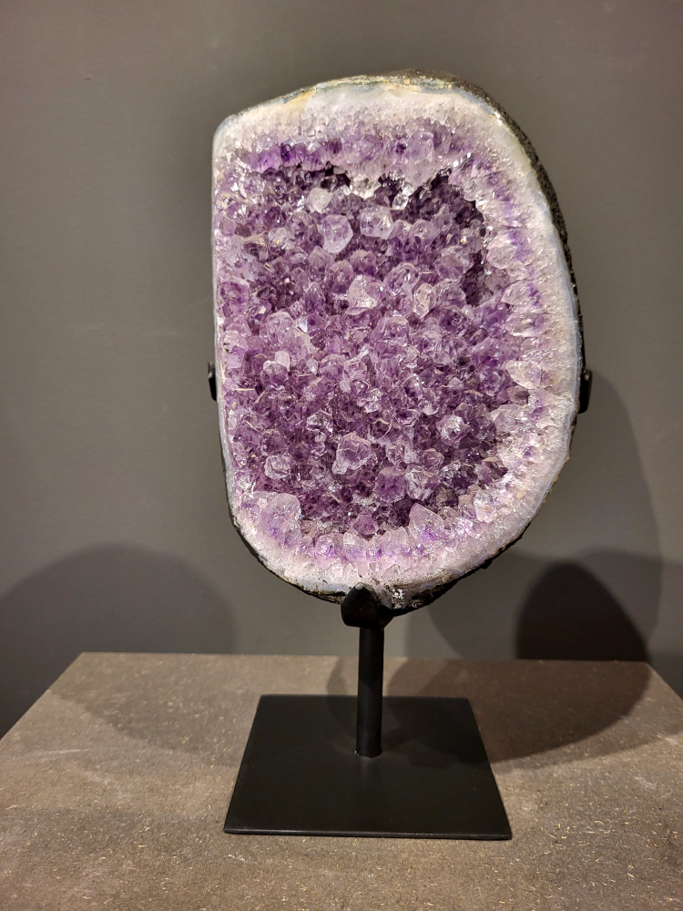 Amethist op standaard, 6,5 kg, 195,- euro, nr. 44
Waar komt amethist vandaan en hoe ontstaan ze?
Amethist wordt wereldwijd gevonden maar de grootste
vondsten worden gedaan in Brazilië, Uruguay, Mexico en Zambia.
Deze edelsteen komt voor in basalt holtes of geodes die ontstaan zijn door
vulkaanuitbarstingen, het duurt miljoenen jaren voordat de kristallen zich vormen.
De kleur van de amethist wordt veroorzaakt door de aanwezigheid
van ijzer en mangaan. 
Waar kan amethist niet goed tegen?
Amethist kan niet goed tegen fel zonlicht en plotselinge
temperatuurwisselingen. Langdurige blootstelling aan zonlicht
doet de kleur doen vervagen en abrupte temperatuur veranderingen
kan voor barsten en/of scheuren zorgen. Amethist kan daarentegen
wel grotendeels tegen water.
Spirituele werking van de amethist:
> Rust, spirituele groei en bescherming.
Amethist staat vooral bekend om zijn kalmerende werking.

                                                                                        -  Kunstgalerie Arnold  - 
