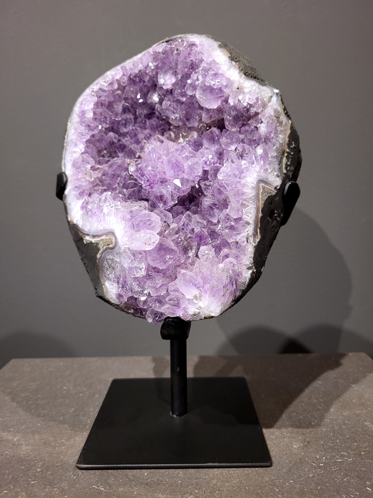 Amethist op standaard, 4,6 kg, 140,- euro, nr. 46 
Waar komt amethist vandaan en hoe ontstaan ze?
Amethist wordt wereldwijd gevonden maar de grootste
vondsten worden gedaan in Brazilië, Uruguay, Mexico en Zambia.
Deze edelsteen komt voor in basalt holtes of geodes die ontstaan zijn door
vulkaanuitbarstingen, het duurt miljoenen jaren voordat de kristallen zich vormen.
De kleur van de amethist wordt veroorzaakt door de aanwezigheid
van ijzer en mangaan. 
Waar kan amethist niet goed tegen?
Amethist kan niet goed tegen fel zonlicht en plotselinge
temperatuurwisselingen. Langdurige blootstelling aan zonlicht
doet de kleur doen vervagen en abrupte temperatuur veranderingen
kan voor barsten en/of scheuren zorgen. Amethist kan daarentegen
wel grotendeels tegen water.
Spirituele werking van de amethist:
> Rust, spirituele groei en bescherming.
Amethist staat vooral bekend om zijn kalmerende werking.

                                                                                        -  Kunstgalerie Arnold  - 