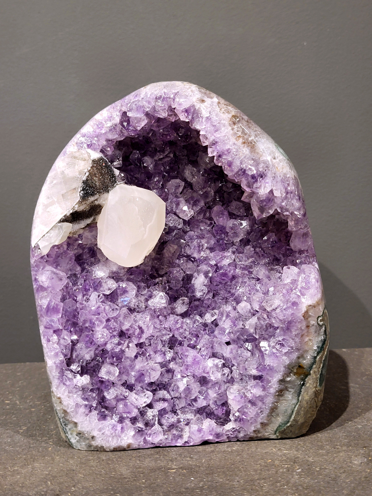 Amethist, met calciet en met standvlak, 3,9 kg, 475,- euro, nr. 21
Waar komt amethist vandaan en hoe ontstaan ze?
Amethist wordt wereldwijd gevonden maar de grootste
vondsten worden gedaan in Brazilië, Uruguay, Mexico en Zambia.
Deze edelsteen komt voor in basalt holtes of geodes die ontstaan zijn door
vulkaanuitbarstingen, het duurt miljoenen jaren voordat de kristallen zich vormen.
De kleur van de amethist wordt veroorzaakt door de aanwezigheid
van ijzer en mangaan. 
Waar kan amethist niet goed tegen?
Amethist kan niet goed tegen fel zonlicht en plotselinge
temperatuurwisselingen. Langdurige blootstelling aan zonlicht
doet de kleur doen vervagen en abrupte temperatuur veranderingen
kan voor barsten en/of scheuren zorgen. Amethist kan daarentegen
wel grotendeels tegen water.
Spirituele werking van de amethist:
> Rust, spirituele groei en bescherming.
Amethist staat vooral bekend om zijn kalmerende werking.

                                                                                        -  Kunstgalerie Arnold  - 