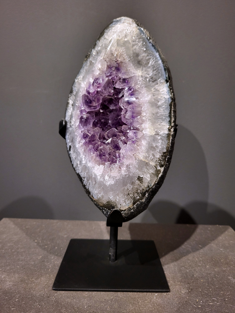 Amethist op standaard, 3,5 kg, 105,- euro, nr. 37 
Waar komt amethist vandaan en hoe ontstaan ze?
Amethist wordt wereldwijd gevonden maar de grootste
vondsten worden gedaan in Brazilië, Uruguay, Mexico en Zambia.
Deze edelsteen komt voor in basalt holtes of geodes die ontstaan zijn door
vulkaanuitbarstingen, het duurt miljoenen jaren voordat de kristallen zich vormen.
De kleur van de amethist wordt veroorzaakt door de aanwezigheid
van ijzer en mangaan. 
Waar kan amethist niet goed tegen?
Amethist kan niet goed tegen fel zonlicht en plotselinge
temperatuurwisselingen. Langdurige blootstelling aan zonlicht
doet de kleur doen vervagen en abrupte temperatuur veranderingen
kan voor barsten en/of scheuren zorgen. Amethist kan daarentegen
wel grotendeels tegen water.
Spirituele werking van de amethist:
> Rust, spirituele groei en bescherming.
Amethist staat vooral bekend om zijn kalmerende werking.

                                                                                        -  Kunstgalerie Arnold  -