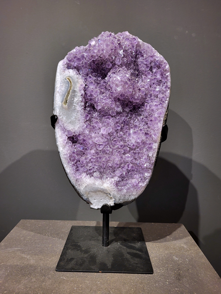Amethist op standaard, 9,2 kg, 275,- euro, nr. 33 
Waar komt amethist vandaan en hoe ontstaan ze?
Amethist wordt wereldwijd gevonden maar de grootste
vondsten worden gedaan in Brazilië, Uruguay, Mexico en Zambia.
Deze edelsteen komt voor in basalt holtes of geodes die ontstaan zijn door
vulkaanuitbarstingen, het duurt miljoenen jaren voordat de kristallen zich vormen.
De kleur van de amethist wordt veroorzaakt door de aanwezigheid
van ijzer en mangaan. 
Waar kan amethist niet goed tegen?
Amethist kan niet goed tegen fel zonlicht en plotselinge
temperatuurwisselingen. Langdurige blootstelling aan zonlicht
doet de kleur doen vervagen en abrupte temperatuur veranderingen
kan voor barsten en/of scheuren zorgen. Amethist kan daarentegen
wel grotendeels tegen water.
Spirituele werking van de amethist:
> Rust, spirituele groei en bescherming.
Amethist staat vooral bekend om zijn kalmerende werking.

                                                                                        -  Kunstgalerie Arnold  - 