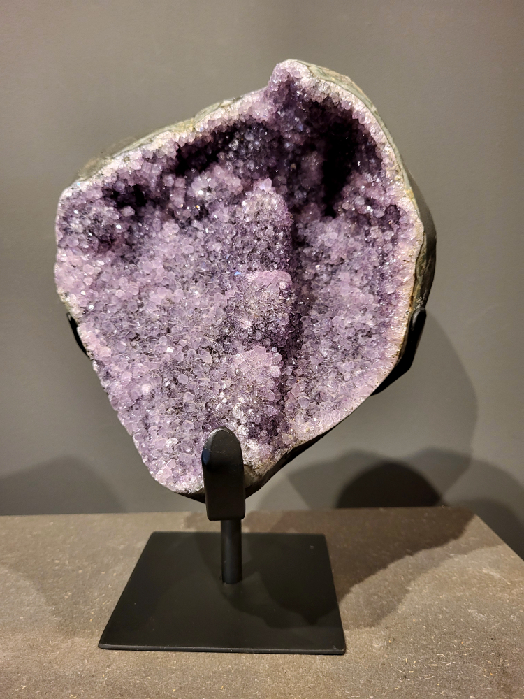 Amethist op standaard, 5,3 kg, 160,- euro, nr. 34 
Waar komt amethist vandaan en hoe ontstaan ze?
Amethist wordt wereldwijd gevonden maar de grootste
vondsten worden gedaan in Brazilië, Uruguay, Mexico en Zambia.
Deze edelsteen komt voor in basalt holtes of geodes die ontstaan zijn door
vulkaanuitbarstingen, het duurt miljoenen jaren voordat de kristallen zich vormen.
De kleur van de amethist wordt veroorzaakt door de aanwezigheid
van ijzer en mangaan. 
Waar kan amethist niet goed tegen?
Amethist kan niet goed tegen fel zonlicht en plotselinge
temperatuurwisselingen. Langdurige blootstelling aan zonlicht
doet de kleur doen vervagen en abrupte temperatuur veranderingen
kan voor barsten en/of scheuren zorgen. Amethist kan daarentegen
wel grotendeels tegen water.
Spirituele werking van de amethist:
> Rust, spirituele groei en bescherming.
Amethist staat vooral bekend om zijn kalmerende werking.

                                                                                        -  Kunstgalerie Arnold  - 