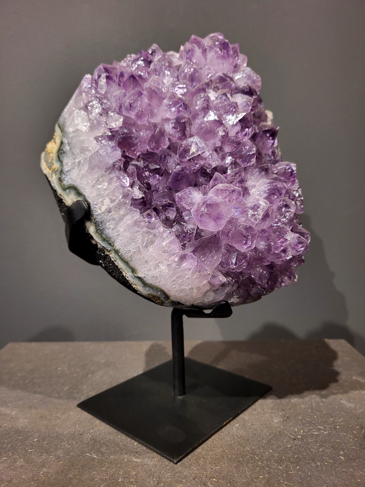 Amethist op standaard, 5,4 kg, 160,- euro, nr. 35
Waar komt amethist vandaan en hoe ontstaan ze?
Amethist wordt wereldwijd gevonden maar de grootste
vondsten worden gedaan in Brazilië, Uruguay, Mexico en Zambia.
Deze edelsteen komt voor in basalt holtes of geodes die ontstaan zijn door
vulkaanuitbarstingen, het duurt miljoenen jaren voordat de kristallen zich vormen.
De kleur van de amethist wordt veroorzaakt door de aanwezigheid
van ijzer en mangaan. 
Waar kan amethist niet goed tegen?
Amethist kan niet goed tegen fel zonlicht en plotselinge
temperatuurwisselingen. Langdurige blootstelling aan zonlicht
doet de kleur doen vervagen en abrupte temperatuur veranderingen
kan voor barsten en/of scheuren zorgen. Amethist kan daarentegen
wel grotendeels tegen water.
Spirituele werking van de amethist:
> Rust, spirituele groei en bescherming.
Amethist staat vooral bekend om zijn kalmerende werking.

                                                                                        -  Kunstgalerie Arnold  - 