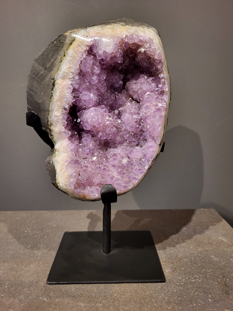 Amethist op standaard, 3,2 kg, 95,- euro, nr. 25 
Waar komt amethist vandaan en hoe ontstaan ze?
Amethist wordt wereldwijd gevonden maar de grootste
vondsten worden gedaan in Brazilië, Uruguay, Mexico en Zambia.
Deze edelsteen komt voor in basalt holtes of geodes die ontstaan zijn door
vulkaanuitbarstingen, het duurt miljoenen jaren voordat de kristallen zich vormen.
De kleur van de amethist wordt veroorzaakt door de aanwezigheid
van ijzer en mangaan. 
Waar kan amethist niet goed tegen?
Amethist kan niet goed tegen fel zonlicht en plotselinge
temperatuurwisselingen. Langdurige blootstelling aan zonlicht
doet de kleur doen vervagen en abrupte temperatuur veranderingen
kan voor barsten en/of scheuren zorgen. Amethist kan daarentegen
wel grotendeels tegen water.
Spirituele werking van de amethist:
> Rust, spirituele groei en bescherming.
Amethist staat vooral bekend om zijn kalmerende werking.

                                                                                        -  Kunstgalerie Arnold  - 