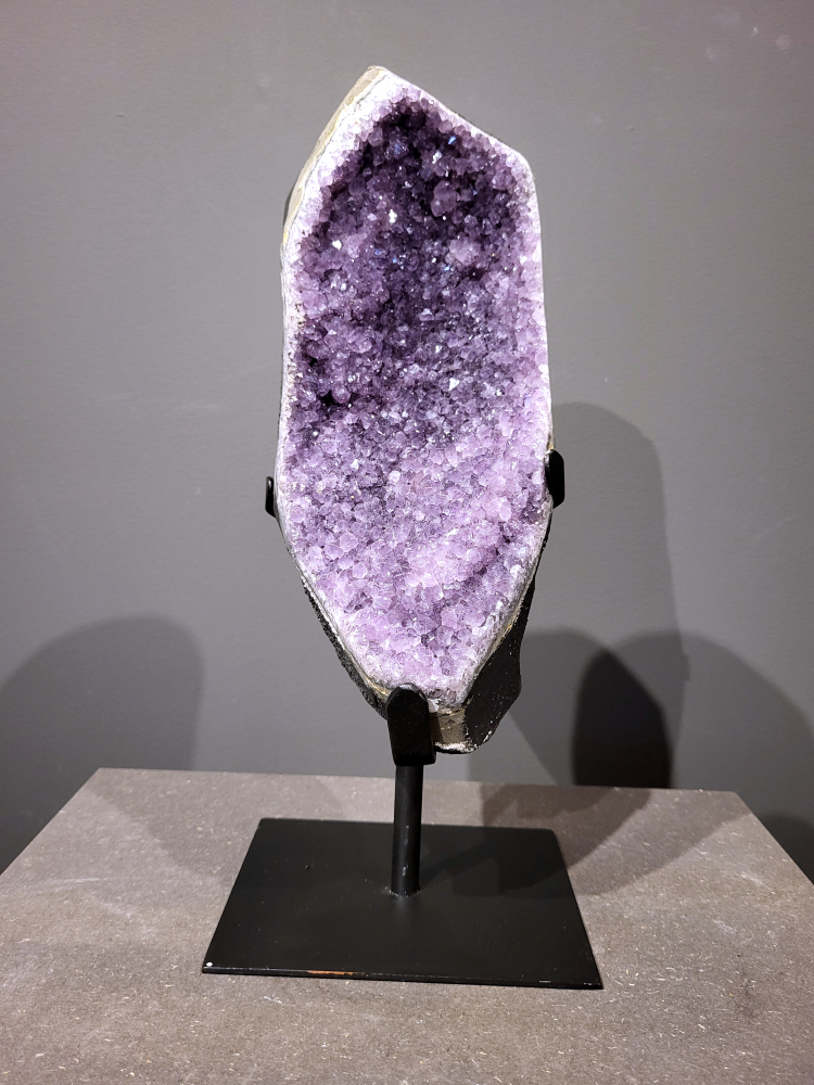 Amethist op standaard, 4,3 kg, 130,- euro, nr. 26
Waar komt amethist vandaan en hoe ontstaan ze?
Amethist wordt wereldwijd gevonden maar de grootste
vondsten worden gedaan in Brazilië, Uruguay, Mexico en Zambia.
Deze edelsteen komt voor in basalt holtes of geodes die ontstaan zijn door
vulkaanuitbarstingen, het duurt miljoenen jaren voordat de kristallen zich vormen.
De kleur van de amethist wordt veroorzaakt door de aanwezigheid
van ijzer en mangaan. 
Waar kan amethist niet goed tegen?
Amethist kan niet goed tegen fel zonlicht en plotselinge
temperatuurwisselingen. Langdurige blootstelling aan zonlicht
doet de kleur doen vervagen en abrupte temperatuur veranderingen
kan voor barsten en/of scheuren zorgen. Amethist kan daarentegen
wel grotendeels tegen water.
Spirituele werking van de amethist:
> Rust, spirituele groei en bescherming.
Amethist staat vooral bekend om zijn kalmerende werking.

                                                                                        -  Kunstgalerie Arnold  - 