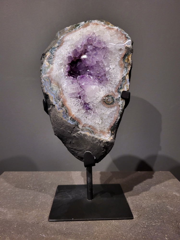 Amethist op standaard, 3,7 kg, hoogte 30cm, 110,- euro, nr. 12
Waar komt amethist vandaan en hoe ontstaan ze?
Amethist wordt wereldwijd gevonden maar de grootste
vondsten worden gedaan in Brazilië, Uruguay, Mexico en Zambia.
Deze edelsteen komt voor in basalt holtes of geodes die ontstaan zijn door
vulkaanuitbarstingen, het duurt miljoenen jaren voordat de kristallen zich vormen.
De kleur van de amethist wordt veroorzaakt door de aanwezigheid
van ijzer en mangaan. 
Waar kan amethist niet goed tegen?
Amethist kan niet goed tegen fel zonlicht en plotselinge
temperatuurwisselingen. Langdurige blootstelling aan zonlicht
doet de kleur doen vervagen en abrupte temperatuur veranderingen
kan voor barsten en/of scheuren zorgen. Amethist kan daarentegen
wel grotendeels tegen water.
Spirituele werking van de amethist:
> Rust, spirituele groei en bescherming.
Amethist staat vooral bekend om zijn kalmerende werking.

                                                                                        -  Kunstgalerie Arnold  - 