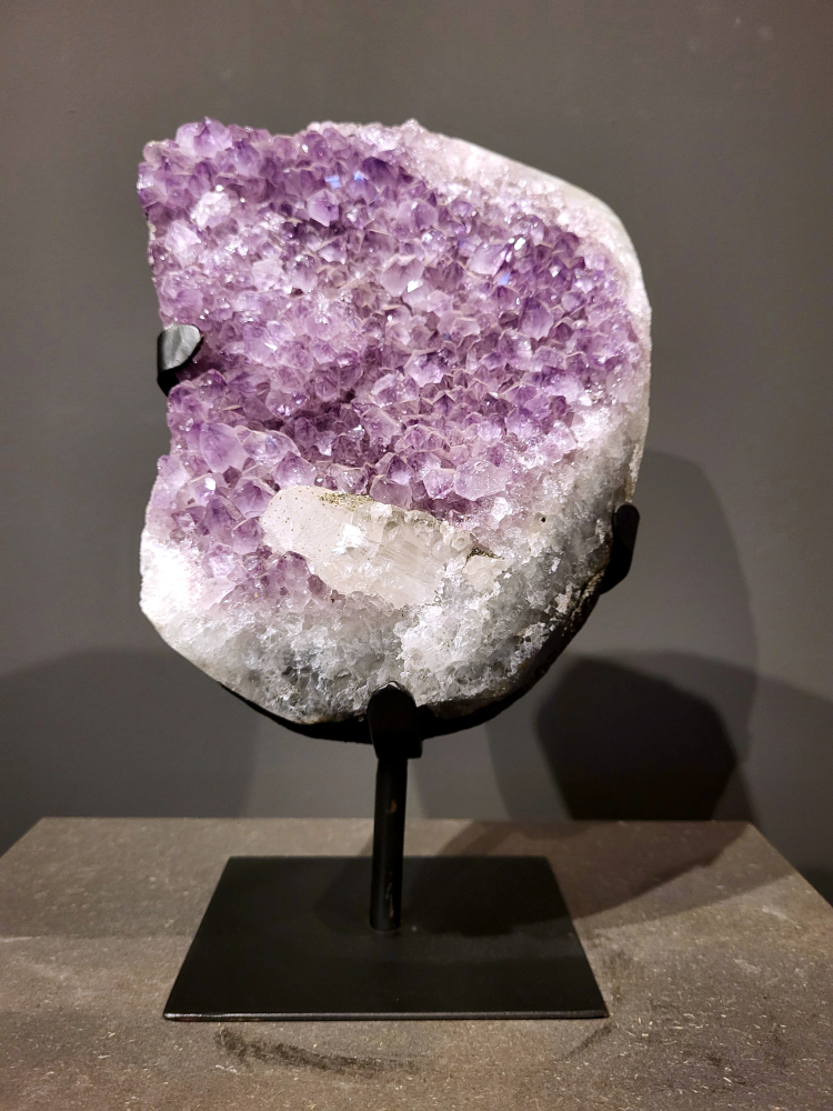 Amethist op standaard, 7,1 kg, 215,- euro, nr. 30
 
Waar komt amethist vandaan en hoe ontstaan ze?
Amethist wordt wereldwijd gevonden maar de grootste
vondsten worden gedaan in Brazilië, Uruguay, Mexico en Zambia.
Deze edelsteen komt voor in basalt holtes of geodes die ontstaan zijn door
vulkaanuitbarstingen, het duurt miljoenen jaren voordat de kristallen zich vormen.
De kleur van de amethist wordt veroorzaakt door de aanwezigheid
van ijzer en mangaan. 
Waar kan amethist niet goed tegen?
Amethist kan niet goed tegen fel zonlicht en plotselinge
temperatuurwisselingen. Langdurige blootstelling aan zonlicht
doet de kleur doen vervagen en abrupte temperatuur veranderingen
kan voor barsten en/of scheuren zorgen. Amethist kan daarentegen
wel grotendeels tegen water.
Spirituele werking van de amethist:
> Rust, spirituele groei en bescherming.
Amethist staat vooral bekend om zijn kalmerende werking.

                                                                                       - Kunstgalerie Arnold  -