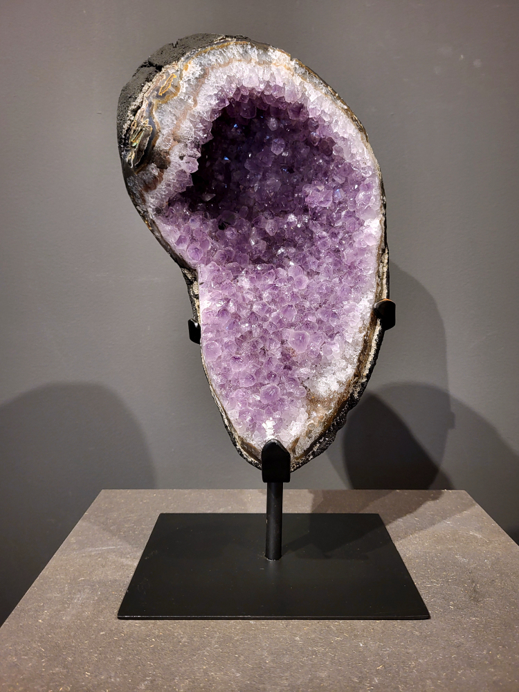 Amethist op standaard, 7,3 kg, 220,- euro, nr. 24
 
Waar komt amethist vandaan en hoe ontstaan ze?
Amethist wordt wereldwijd gevonden maar de grootste
vondsten worden gedaan in Brazilië, Uruguay, Mexico en Zambia.
Deze edelsteen komt voor in basalt holtes of geodes die ontstaan zijn door
vulkaanuitbarstingen, het duurt miljoenen jaren voordat de kristallen zich vormen.
De kleur van de amethist wordt veroorzaakt door de aanwezigheid
van ijzer en mangaan. 
Waar kan amethist niet goed tegen?
Amethist kan niet goed tegen fel zonlicht en plotselinge
temperatuurwisselingen. Langdurige blootstelling aan zonlicht
doet de kleur doen vervagen en abrupte temperatuur veranderingen
kan voor barsten en/of scheuren zorgen. Amethist kan daarentegen
wel grotendeels tegen water.
Spirituele werking van de amethist:
> Rust, spirituele groei en bescherming.
Amethist staat vooral bekend om zijn kalmerende werking.

                                                                                        -  Kunstgalerie Arnold  - 
