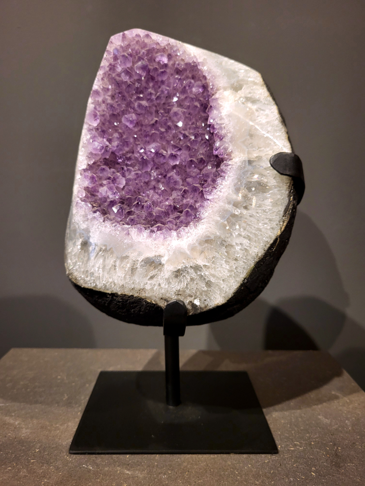 Amethist op standaard, 8,1 kg, 245,- euro, nr. 31
Waar komt amethist vandaan en hoe ontstaan ze?
Amethist wordt wereldwijd gevonden maar de grootste
vondsten worden gedaan in Brazilië, Uruguay, Mexico en Zambia.
Deze edelsteen komt voor in basalt holtes of geodes die ontstaan zijn door
vulkaanuitbarstingen, het duurt miljoenen jaren voordat de kristallen zich vormen.
De kleur van de amethist wordt veroorzaakt door de aanwezigheid
van ijzer en mangaan. 
Waar kan amethist niet goed tegen?
Amethist kan niet goed tegen fel zonlicht en plotselinge
temperatuurwisselingen. Langdurige blootstelling aan zonlicht
doet de kleur doen vervagen en abrupte temperatuur veranderingen
kan voor barsten en/of scheuren zorgen. Amethist kan daarentegen
wel grotendeels tegen water.
Spirituele werking van de amethist:
> Rust, spirituele groei en bescherming.
Amethist staat vooral bekend om zijn kalmerende werking.

                                                                                        -  Kunstgalerie Arnold  - 