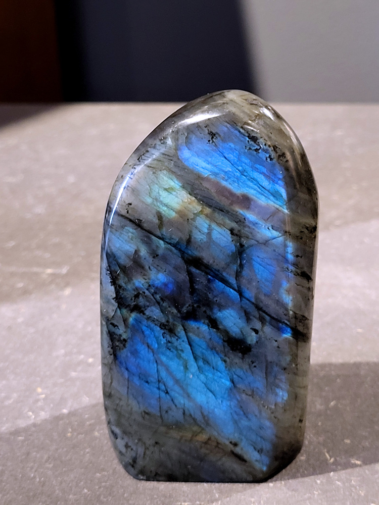 Labradoriet, 0,3kg, 9cm hoog, 16,- euro, nr. 55
Beschrijving, Labradoriet.
Labradoriet is een edelsteen die bekend staat om zijn iriserende kleurenspel, ook wel labradoriseren genoemd, dat vaak doet denken aan het noorderlicht. Het is een populaire steen in de edelstenenwereld vanwege zowel zijn uiterlijk als zijn vermeende spirituele eigenschappen. 
Wat is labradoriet?
Labradoriet is een veldspaatmineraal dat wordt gekenmerkt door een opaalachtig glans of iriserend effect, veroorzaakt door de lichtbreking in de interne structuur van de steen.
De meest voorkomende kleur is grijs of groenachtig grijs, maar de steen kan ook blauwe, gele, oranje, paarse of zelfs rode flitsen laten zien.
De steen is genoemd naar het Canadese schiereiland Labrador, waar het voor het eerst werd ontdekt. 
Spirituele betekenis en eigenschappen:
Labradoriet wordt vaak beschouwd als een beschermende steen, vooral voor mensen die gevoelig zijn voor de energieën van hun omgeving. 
Het zou helpen bij het versterken van de aura en het verminderen van energielekkage, waardoor je je weerbaarder voelt. 
Labradoriet wordt geassocieerd met het versterken van intuïtie, het vergroten van het bewustzijn en het transformeren van negatieve energieën. 
Het wordt ook gebruikt om blokkades op te heffen en de innerlijke wijsheid te onthullen. 
Gebruik:
Labradoriet wordt vaak verwerkt in sieraden zoals hangers, armbanden en oorbellen. 
Het kan ook als ruwe steen, knuffelsteen of in andere vormen worden gebruikt, bijvoorbeeld in een huis of op een werkplek. 
Labradoriet kan worden gereinigd door het onder stromend water te houden of door het te reinigen met een andere steen zoals bergkristal of seleniet. 
Vindplaatsen:
Labradoriet wordt gevonden op verschillende locaties over de hele wereld, waaronder Canada, Finland, Madagaskar en Rusland. 
                                -Kunstgalerie Arnold-