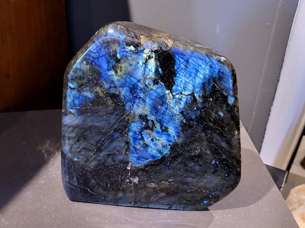 Labradoriet, 7,7kg, 22cm hoog, 270,- euro, nr. 7
Beschrijving, Labradoriet.
Labradoriet is een edelsteen die bekend staat om zijn iriserende kleurenspel, ook wel labradoriseren genoemd, dat vaak doet denken aan het noorderlicht. Het is een populaire steen in de edelstenenwereld vanwege zowel zijn uiterlijk als zijn vermeende spirituele eigenschappen. 
Wat is labradoriet?
Labradoriet is een veldspaatmineraal dat wordt gekenmerkt door een opaalachtig glans of iriserend effect, veroorzaakt door de lichtbreking in de interne structuur van de steen.
De meest voorkomende kleur is grijs of groenachtig grijs, maar de steen kan ook blauwe, gele, oranje, paarse of zelfs rode flitsen laten zien.
De steen is genoemd naar het Canadese schiereiland Labrador, waar het voor het eerst werd ontdekt. 
Spirituele betekenis en eigenschappen:
Labradoriet wordt vaak beschouwd als een beschermende steen, vooral voor mensen die gevoelig zijn voor de energieën van hun omgeving. 
Het zou helpen bij het versterken van de aura en het verminderen van energielekkage, waardoor je je weerbaarder voelt. 
Labradoriet wordt geassocieerd met het versterken van intuïtie, het vergroten van het bewustzijn en het transformeren van negatieve energieën. 
Het wordt ook gebruikt om blokkades op te heffen en de innerlijke wijsheid te onthullen. 
Gebruik:
Labradoriet wordt vaak verwerkt in sieraden zoals hangers, armbanden en oorbellen. 
Het kan ook als ruwe steen, knuffelsteen of in andere vormen worden gebruikt, bijvoorbeeld in een huis of op een werkplek. 
Labradoriet kan worden gereinigd door het onder stromend water te houden of door het te reinigen met een andere steen zoals bergkristal of seleniet. 
Vindplaatsen:
Labradoriet wordt gevonden op verschillende locaties over de hele wereld, waaronder Canada, Finland, Madagaskar en Rusland. 
-kunstgalerie-arnold-