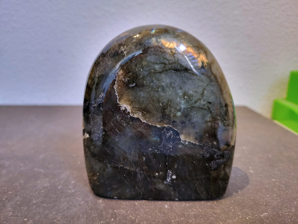 Labradoriet, 0,7kg, 10cm hoog, 21,- euro, nr. 28
Beschrijving, Labradoriet.
Labradoriet is een edelsteen die bekend staat om zijn iriserende kleurenspel, ook wel labradoriseren genoemd, dat vaak doet denken aan het noorderlicht. Het is een populaire steen in de edelstenenwereld vanwege zowel zijn uiterlijk als zijn vermeende spirituele eigenschappen. 
Wat is labradoriet?
Labradoriet is een veldspaatmineraal dat wordt gekenmerkt door een opaalachtig glans of iriserend effect, veroorzaakt door de lichtbreking in de interne structuur van de steen.
De meest voorkomende kleur is grijs of groenachtig grijs, maar de steen kan ook blauwe, gele, oranje, paarse of zelfs rode flitsen laten zien.
De steen is genoemd naar het Canadese schiereiland Labrador, waar het voor het eerst werd ontdekt. 
Spirituele betekenis en eigenschappen:
Labradoriet wordt vaak beschouwd als een beschermende steen, vooral voor mensen die gevoelig zijn voor de energieën van hun omgeving. 
Het zou helpen bij het versterken van de aura en het verminderen van energielekkage, waardoor je je weerbaarder voelt. 
Labradoriet wordt geassocieerd met het versterken van intuïtie, het vergroten van het bewustzijn en het transformeren van negatieve energieën. 
Het wordt ook gebruikt om blokkades op te heffen en de innerlijke wijsheid te onthullen. 
Gebruik:
Labradoriet wordt vaak verwerkt in sieraden zoals hangers, armbanden en oorbellen. 
Het kan ook als ruwe steen, knuffelsteen of in andere vormen worden gebruikt, bijvoorbeeld in een huis of op een werkplek. 
Labradoriet kan worden gereinigd door het onder stromend water te houden of door het te reinigen met een andere steen zoals bergkristal of seleniet. 
Vindplaatsen:
Labradoriet wordt gevonden op verschillende locaties over de hele wereld, waaronder Canada, Finland, Madagaskar en Rusland. 
                                -Kunstgalerie Arnold-