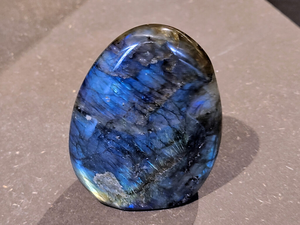 Labradoriet, 0,2kg, 7cm hoog, 10,- euro, nr. 24
Beschrijving, Labradoriet.
Labradoriet is een edelsteen die bekend staat om zijn iriserende kleurenspel, ook wel labradoriseren genoemd, dat vaak doet denken aan het noorderlicht. Het is een populaire steen in de edelstenenwereld vanwege zowel zijn uiterlijk als zijn vermeende spirituele eigenschappen. 
Wat is labradoriet?
Labradoriet is een veldspaatmineraal dat wordt gekenmerkt door een opaalachtig glans of iriserend effect, veroorzaakt door de lichtbreking in de interne structuur van de steen.
De meest voorkomende kleur is grijs of groenachtig grijs, maar de steen kan ook blauwe, gele, oranje, paarse of zelfs rode flitsen laten zien.
De steen is genoemd naar het Canadese schiereiland Labrador, waar het voor het eerst werd ontdekt. 
Spirituele betekenis en eigenschappen:
Labradoriet wordt vaak beschouwd als een beschermende steen, vooral voor mensen die gevoelig zijn voor de energieën van hun omgeving. 
Het zou helpen bij het versterken van de aura en het verminderen van energielekkage, waardoor je je weerbaarder voelt. 
Labradoriet wordt geassocieerd met het versterken van intuïtie, het vergroten van het bewustzijn en het transformeren van negatieve energieën. 
Het wordt ook gebruikt om blokkades op te heffen en de innerlijke wijsheid te onthullen. 
Gebruik:
Labradoriet wordt vaak verwerkt in sieraden zoals hangers, armbanden en oorbellen. 
Het kan ook als ruwe steen, knuffelsteen of in andere vormen worden gebruikt, bijvoorbeeld in een huis of op een werkplek. 
Labradoriet kan worden gereinigd door het onder stromend water te houden of door het te reinigen met een andere steen zoals bergkristal of seleniet. 
Vindplaatsen:
Labradoriet wordt gevonden op verschillende locaties over de hele wereld, waaronder Canada, Finland, Madagaskar en Rusland. 
                                -Kunstgalerie Arnold-