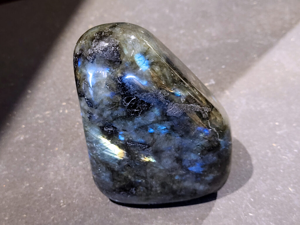 Labradoriet, 0,6kg, 11cm hoog, 19,- euro, nr. 20
Beschrijving, Labradoriet.
Labradoriet is een edelsteen die bekend staat om zijn iriserende kleurenspel, ook wel labradoriseren genoemd, dat vaak doet denken aan het noorderlicht. Het is een populaire steen in de edelstenenwereld vanwege zowel zijn uiterlijk als zijn vermeende spirituele eigenschappen. 
Wat is labradoriet?
Labradoriet is een veldspaatmineraal dat wordt gekenmerkt door een opaalachtig glans of iriserend effect, veroorzaakt door de lichtbreking in de interne structuur van de steen.
De meest voorkomende kleur is grijs of groenachtig grijs, maar de steen kan ook blauwe, gele, oranje, paarse of zelfs rode flitsen laten zien.
De steen is genoemd naar het Canadese schiereiland Labrador, waar het voor het eerst werd ontdekt. 
Spirituele betekenis en eigenschappen:
Labradoriet wordt vaak beschouwd als een beschermende steen, vooral voor mensen die gevoelig zijn voor de energieën van hun omgeving. 
Het zou helpen bij het versterken van de aura en het verminderen van energielekkage, waardoor je je weerbaarder voelt. 
Labradoriet wordt geassocieerd met het versterken van intuïtie, het vergroten van het bewustzijn en het transformeren van negatieve energieën. 
Het wordt ook gebruikt om blokkades op te heffen en de innerlijke wijsheid te onthullen. 
Gebruik:
Labradoriet wordt vaak verwerkt in sieraden zoals hangers, armbanden en oorbellen. 
Het kan ook als ruwe steen, knuffelsteen of in andere vormen worden gebruikt, bijvoorbeeld in een huis of op een werkplek. 
Labradoriet kan worden gereinigd door het onder stromend water te houden of door het te reinigen met een andere steen zoals bergkristal of seleniet. 
Vindplaatsen:
Labradoriet wordt gevonden op verschillende locaties over de hele wereld, waaronder Canada, Finland, Madagaskar en Rusland. 
                                -Kunstgalerie Arnold-